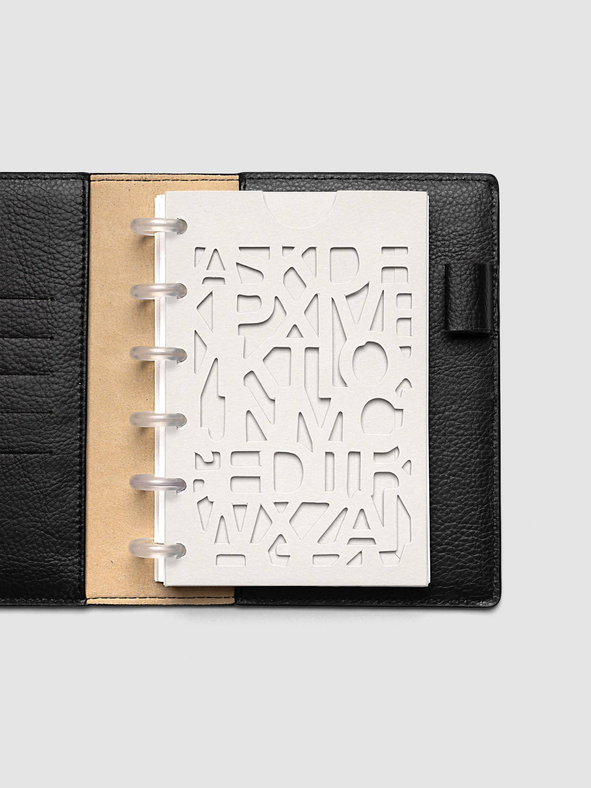The CP Petite 6-Disc Punch Diecut Pocket Folder empty at the front of a black leather ring bound planner, the cut letters showing the blank page beneath