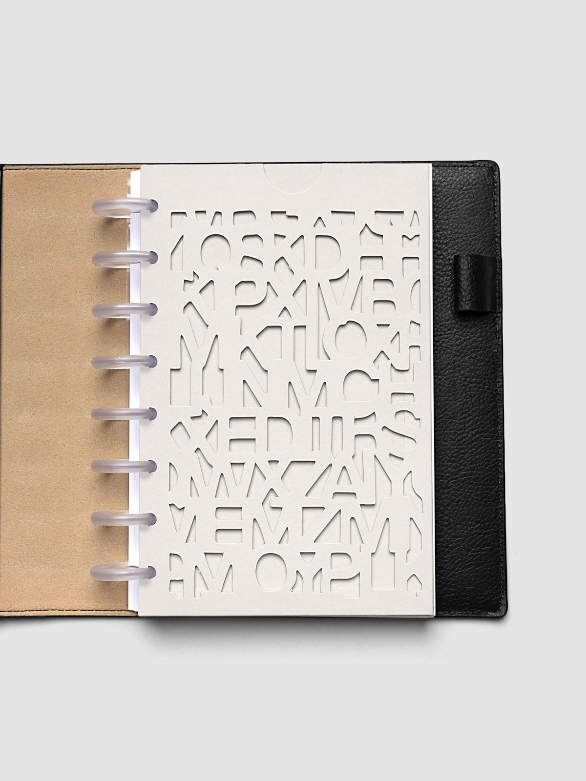 The Half Letter 8-Disc Punch Diecut Pocket Folder empty at the front of a black leather ring bound planner, the cut letters showing the blank page beneath