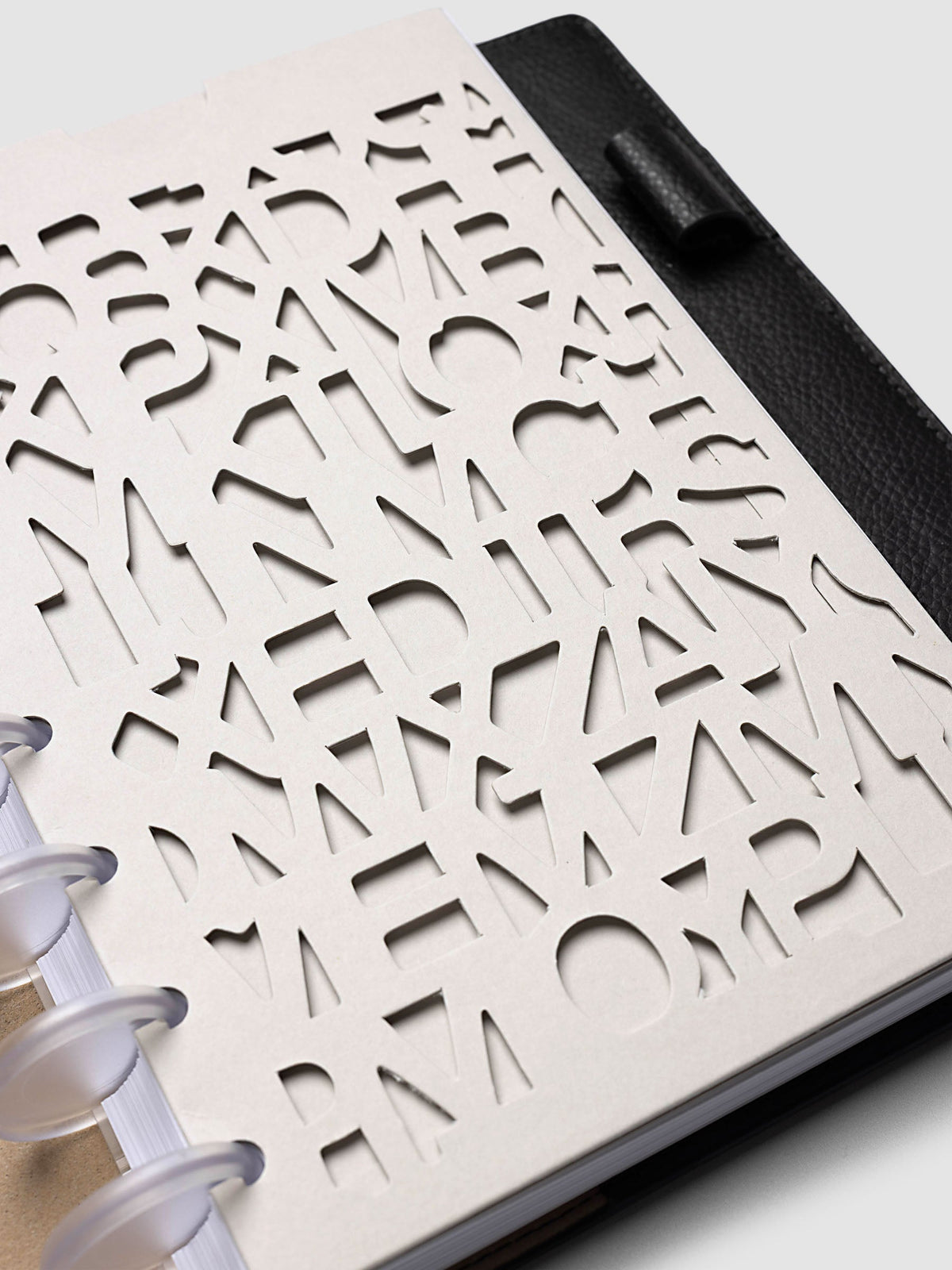 Close-up of the Half Letter 8-Disc Punch Diecut Pocket Folder at an angle on a black pebbled leather cover, showing the depth of the cut letters and the printed logo along the edge of the solid back panel