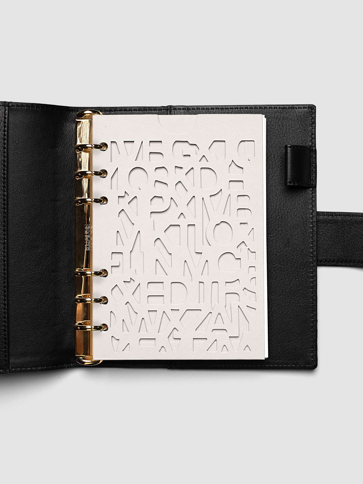 The Personal Wide Diecut Pocket Folder empty at the front of a black leather ring bound planner, the cut letters showing the blank page beneath