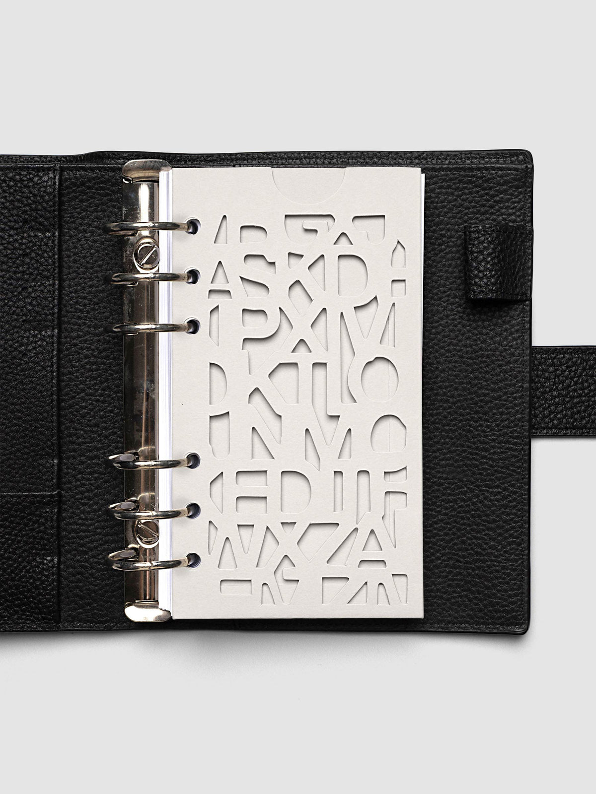 The Personal Diecut Pocket Folder empty at the front of a black leather ring bound planner, the cut letters showing the blank page beneath
