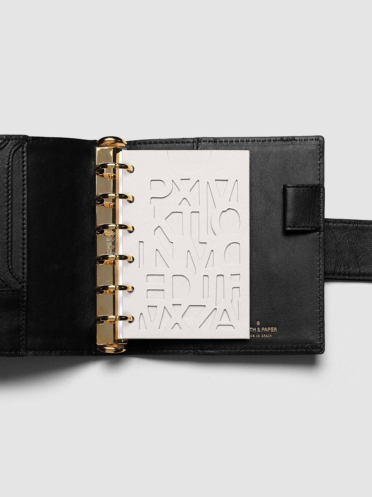 The Pocket Diecut Pocket Folder empty at the front of a black leather ring bound planner, the cut letters showing the blank page beneath