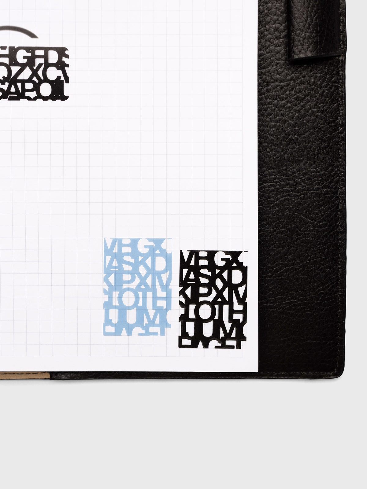 Label Stickers | Precision applied to a graph paper page in a black leather planner, one Hyacinth sticker beside one Avant Garde sticker