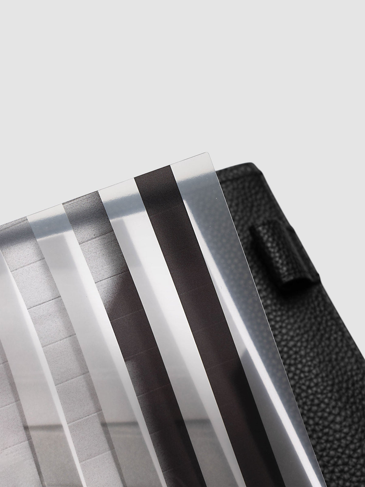 Close-up of the top corner of the clear plastic layer of the A5 6-Ring Punch Strips Planner Dashboard Duo, showing the alternating clear and printed strips against a black pebbled leather cover