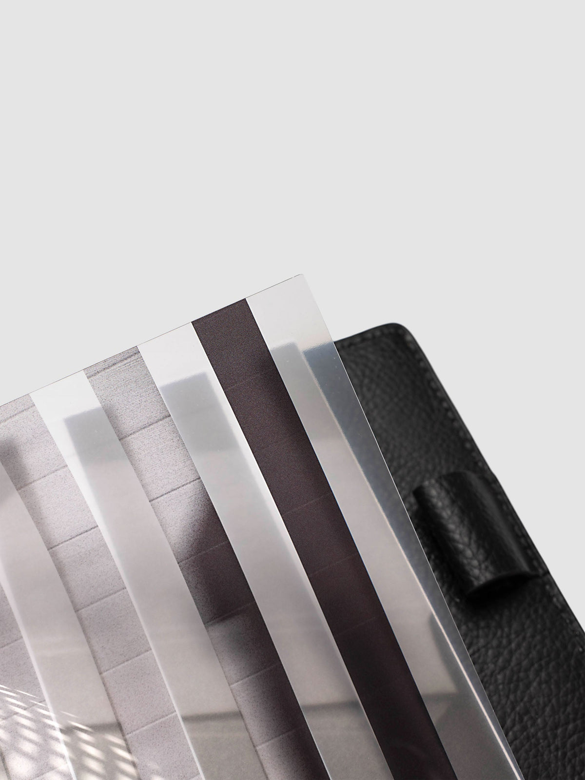 Close-up of the top corner of the clear plastic layer of the Half Letter 8-Disc Punch Strips Planner Dashboard Duo, showing the alternating clear and printed strips against a black pebbled leather cover