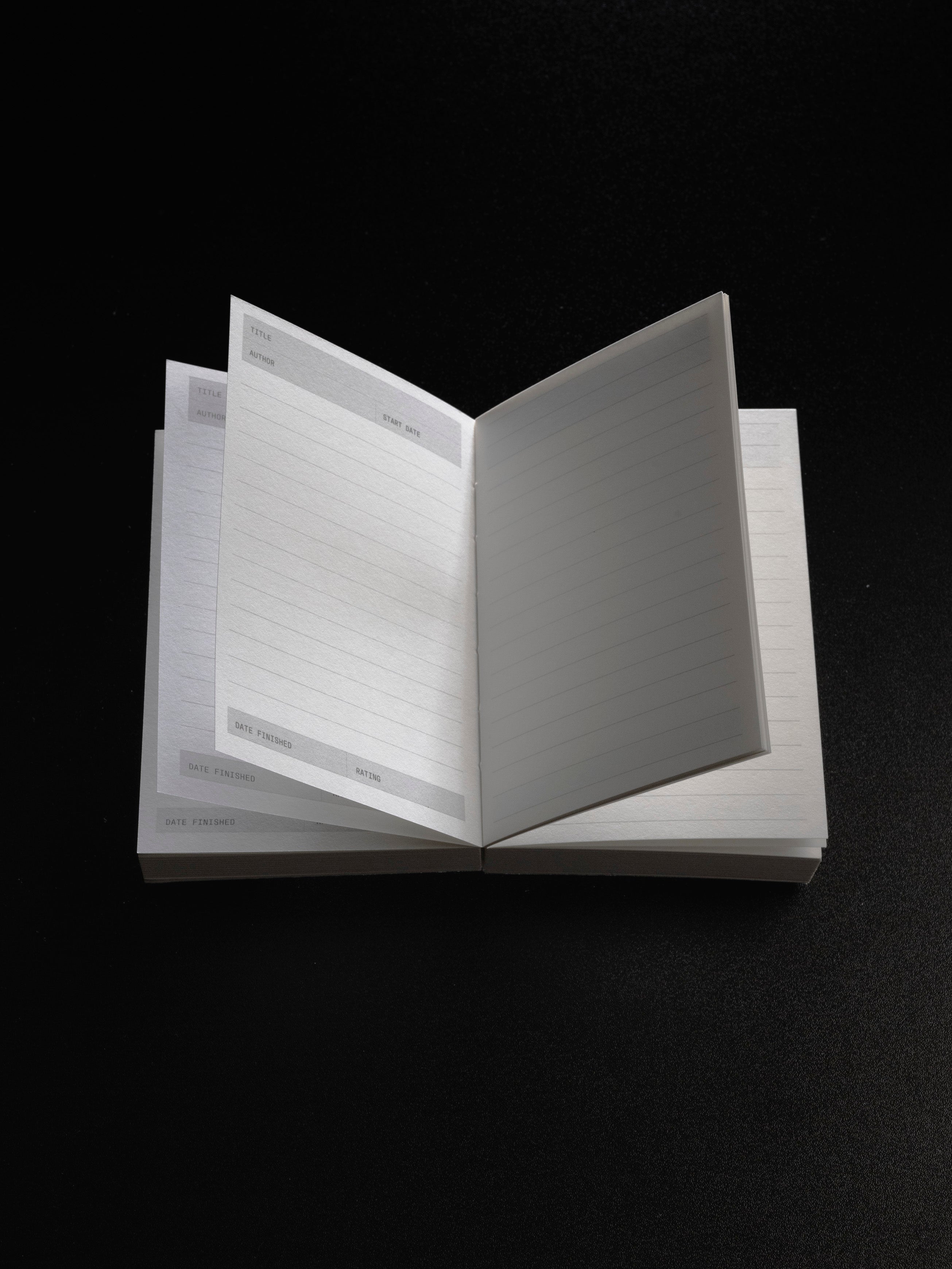 Bibliophile Notebook open on a black surface, showing vellum and printed pages with fields for title, author, start date, date finished, and rating.