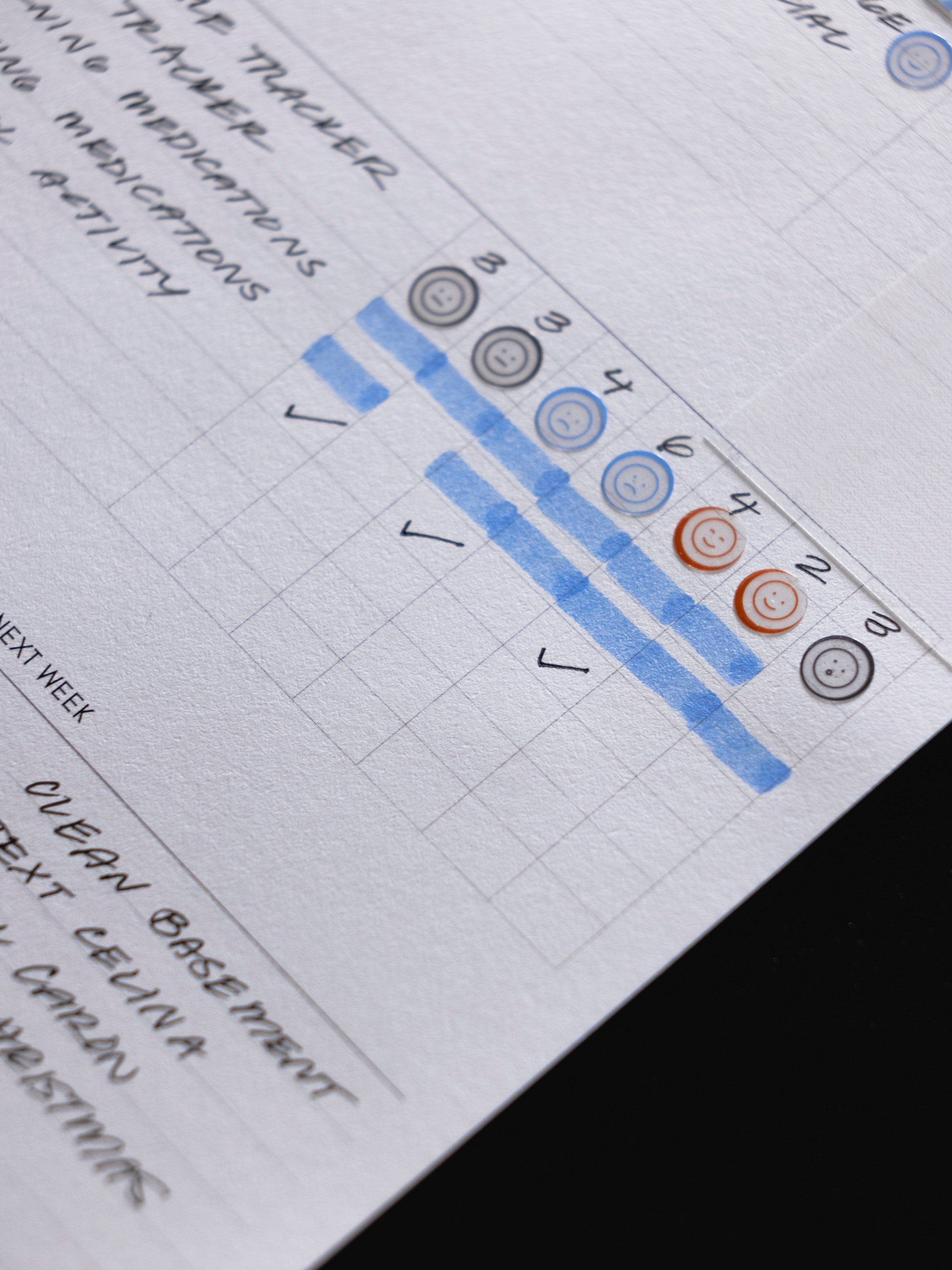 Close angled view of the Weekly Essentials insert filled in by hand, showing a tracker column marked with highlighter and a row of Icon Stickers applied down the edge.