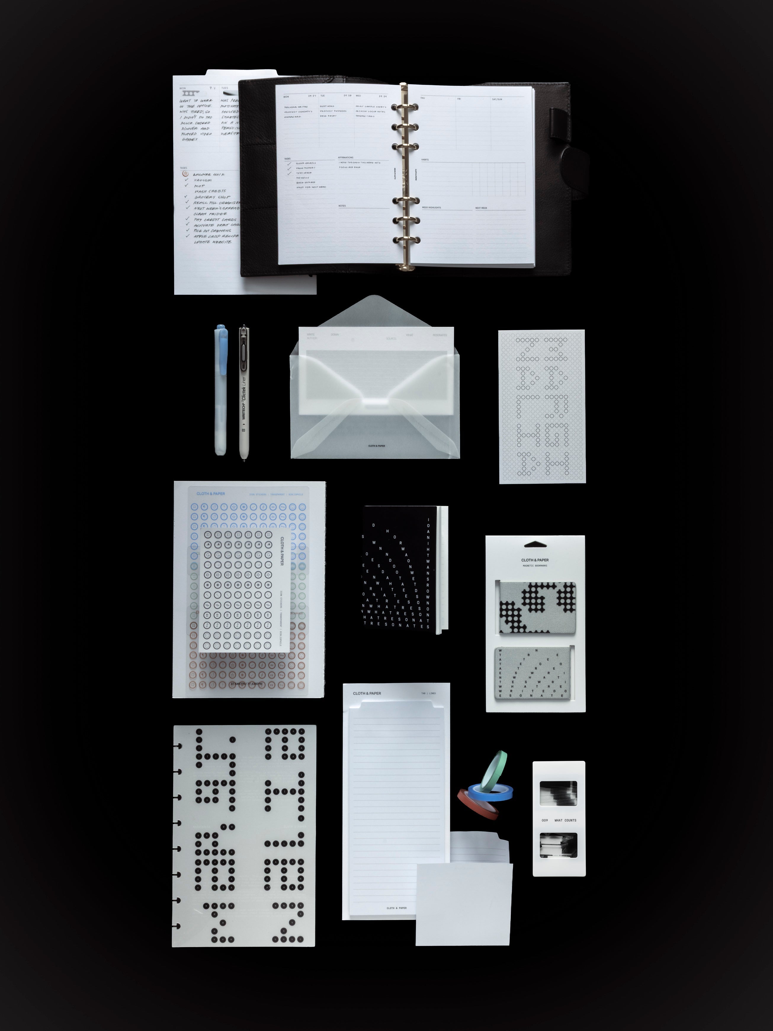 Overhead view of the full September Intention Box contents on a black surface, including a six ring planner open to the Weekly Essentials insert, a highlighter and a fine liner pen, Archive Index Cards in a vellum envelope, Icon Stickers in four colorways, the Bibliophile Notebook, Magnetic Bookmarks, a Scantron dashboard, Large Sticky Notes, Annotation Tape, and a Scantron Photo Slide.