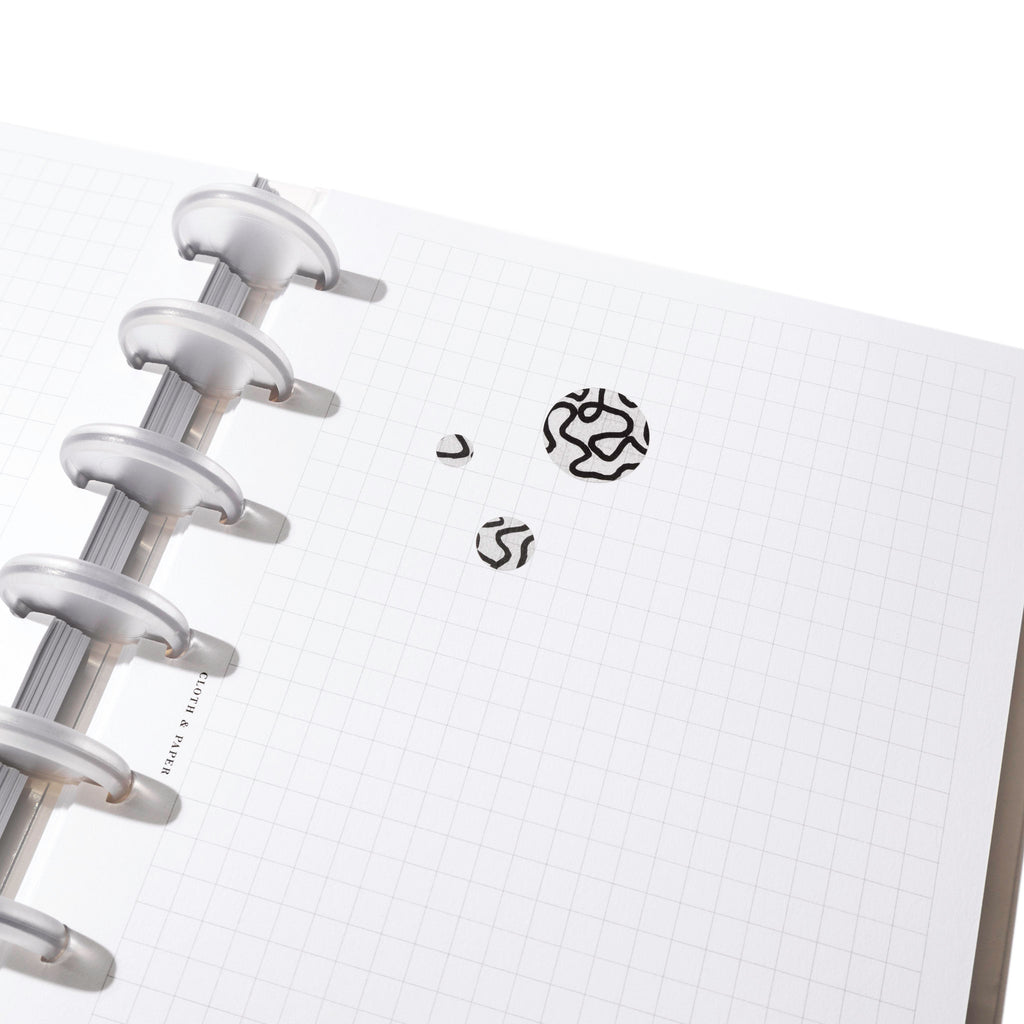 A small, medium, and large sticker are pressed onto a page in a discbound planner.