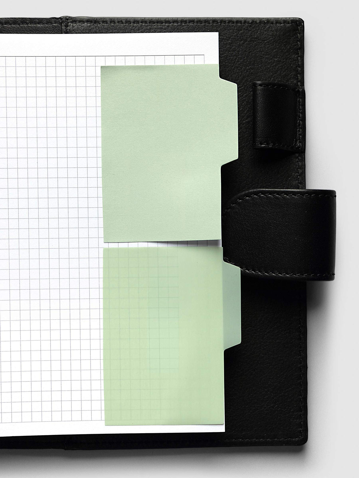 Blank Tab Sticky Note Set, Matcha, Cloth and Paper. One transparent and one matte note from the set placed on a grid insert in a black leather planner.