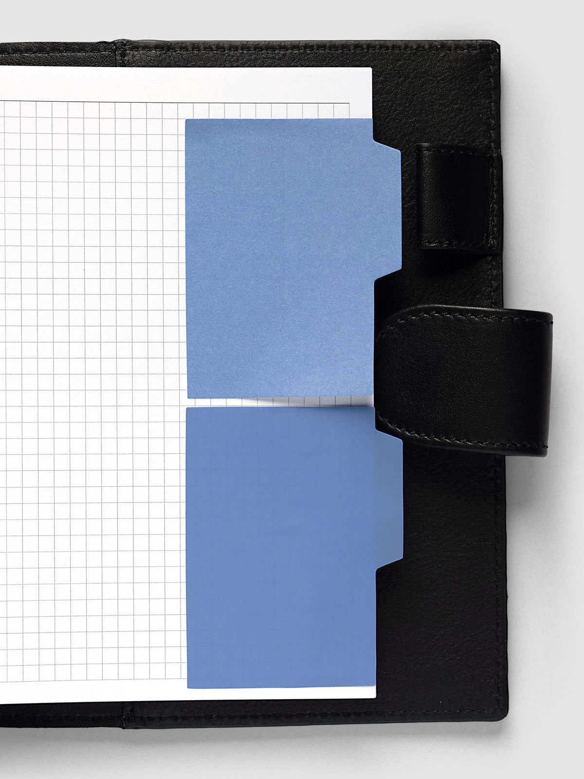 Blank Tab Sticky Note Set, Santorini, Cloth and Paper. One transparent and one matte note from the set placed on a grid insert in a black leather planner.