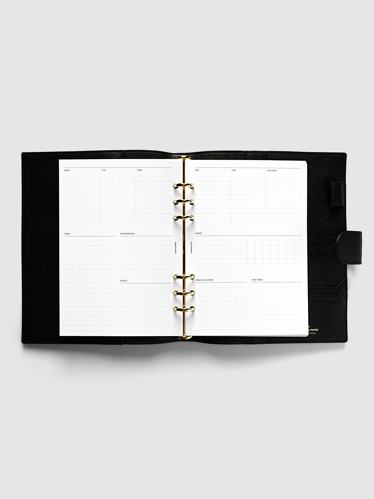 Weekly Essentials Planner Inserts, A5 6-Ring Punch, weekly spread open on the gold rings of a black leather planner, daily columns across the top and weekly sections below