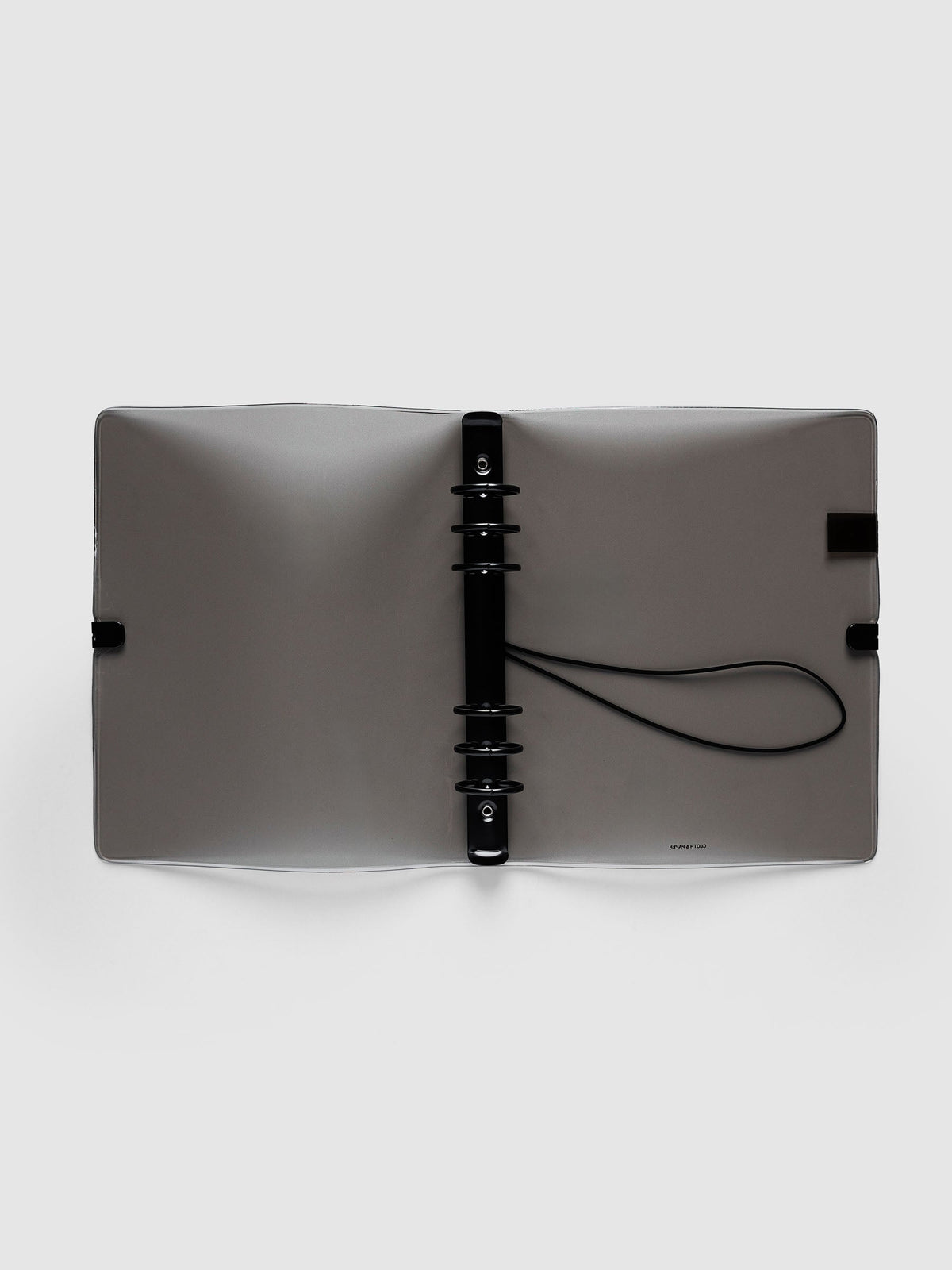 Ring Cover in black tinted vinyl, A5 6-Ring Punch, open flat showing the black six-ring mechanism, the black bungee cord and the printed logo