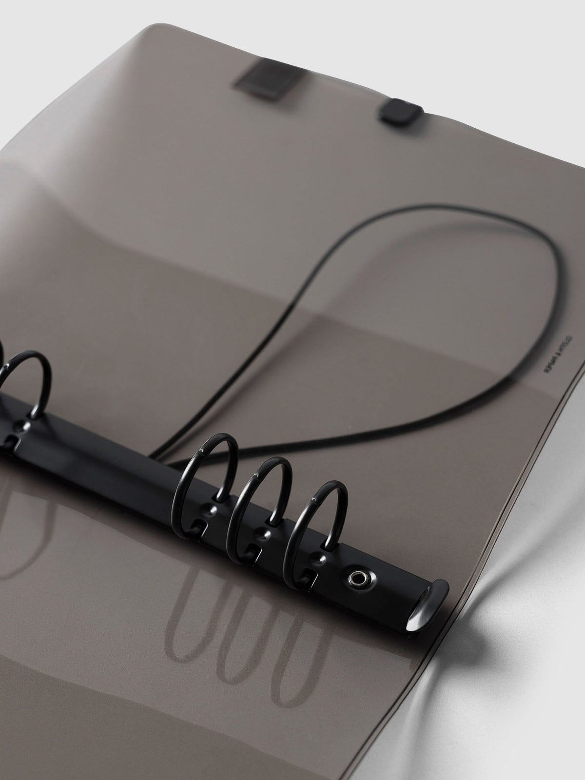 Angled close-up of the black six-ring mechanism and black bungee cord inside the A5 6-Ring Punch Ring Cover in black tinted vinyl