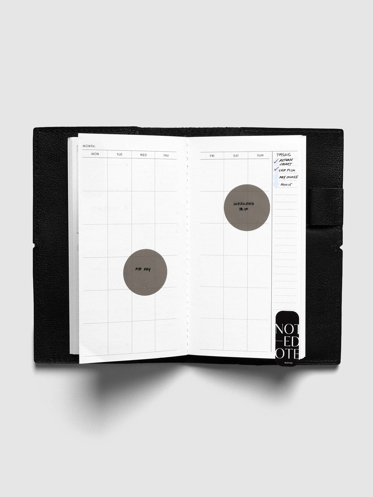 Monthly Overview Pocket Plus calendar spread inside a black travel notebook cover, with PTO Day and Weekend Trip circle stickers, a task list and a Noted sticker