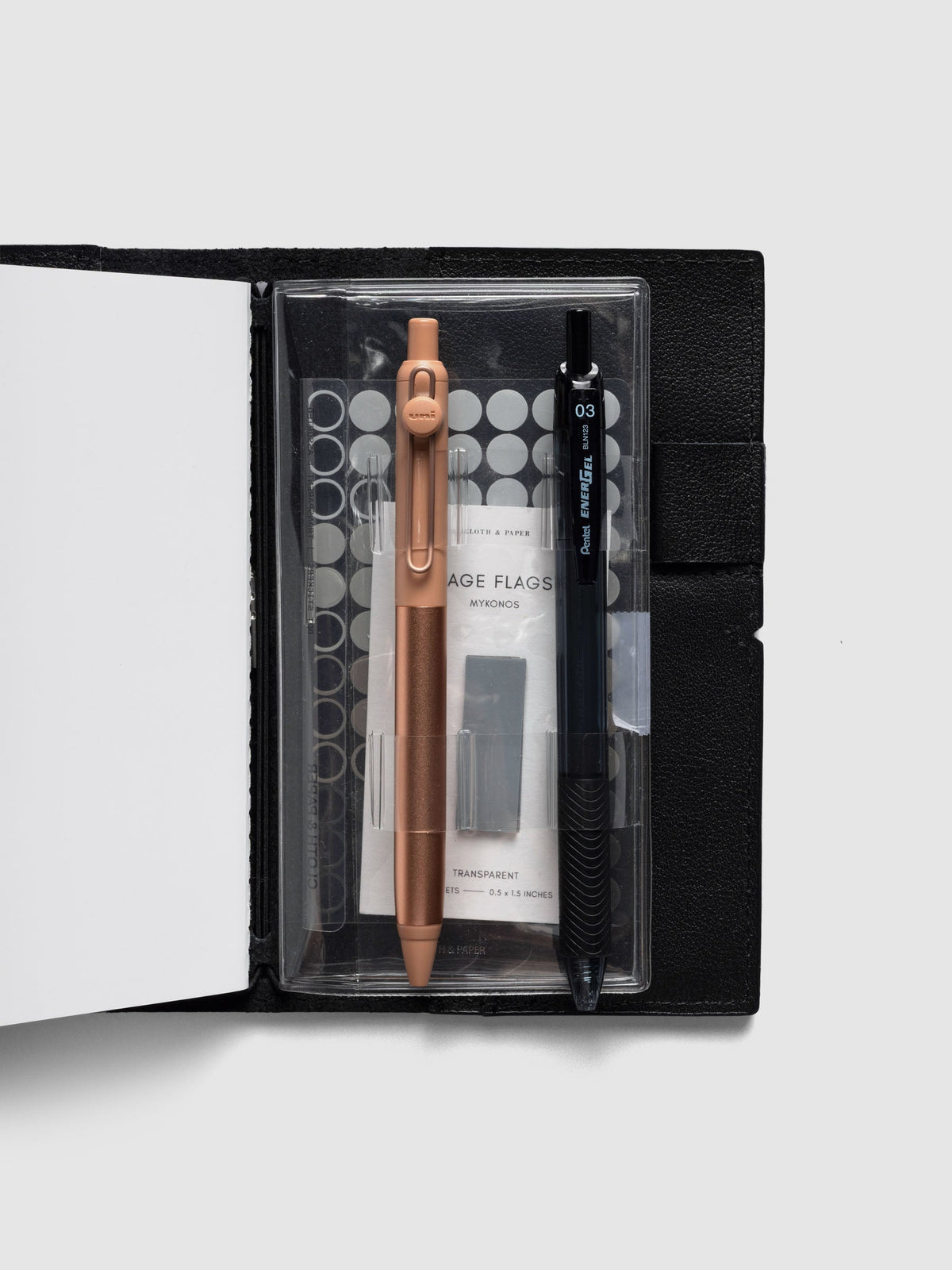 Travel Tool Kit, Pocket Plus, inside a black travel notebook, holding a copper and a black gel pen over dot stickers and page flags