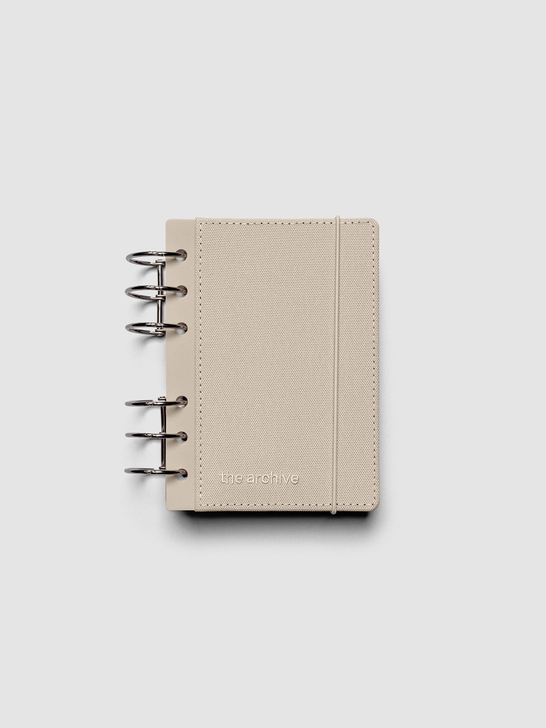 A6 ring bound planner with a beige bookcloth cover against a grey background.