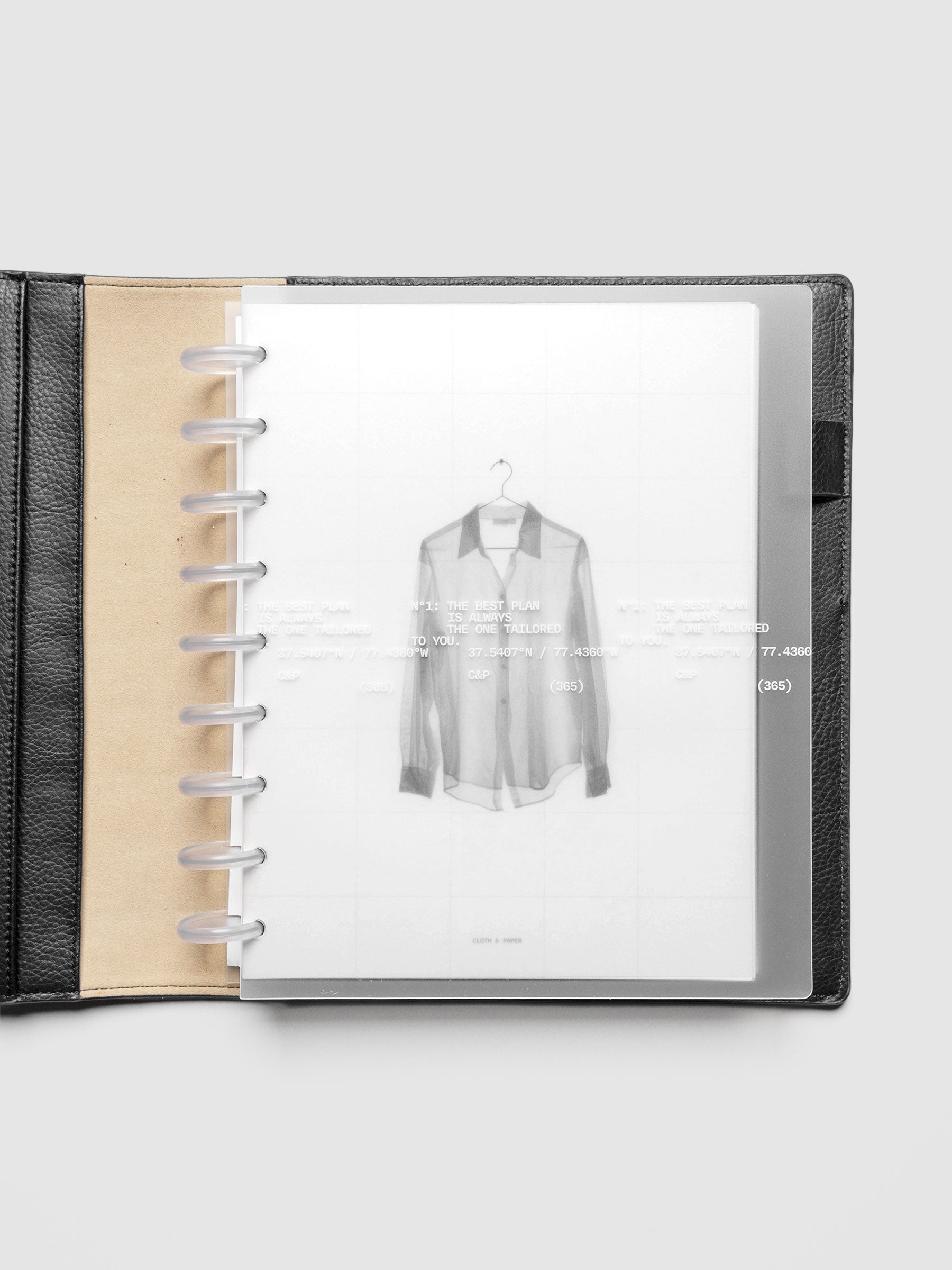 Transparent planner cover set with white printed text design and accompanying black and white dashboard with an image of a tailored shirt on a hanger. Shown discbound in a black leather folio in size HP Classic.