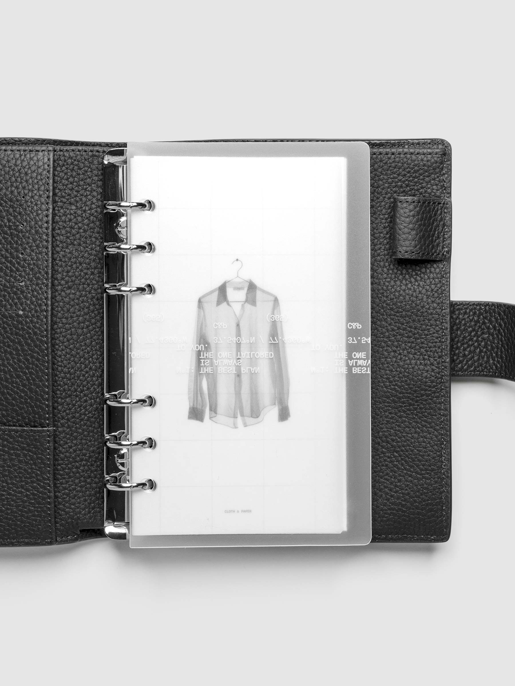 Transparent planner cover set with white printed text design and accompanying black and white dashboard with an image of a tailored shirt on a hanger. Shown bound in a black leather agenda in size Personal.