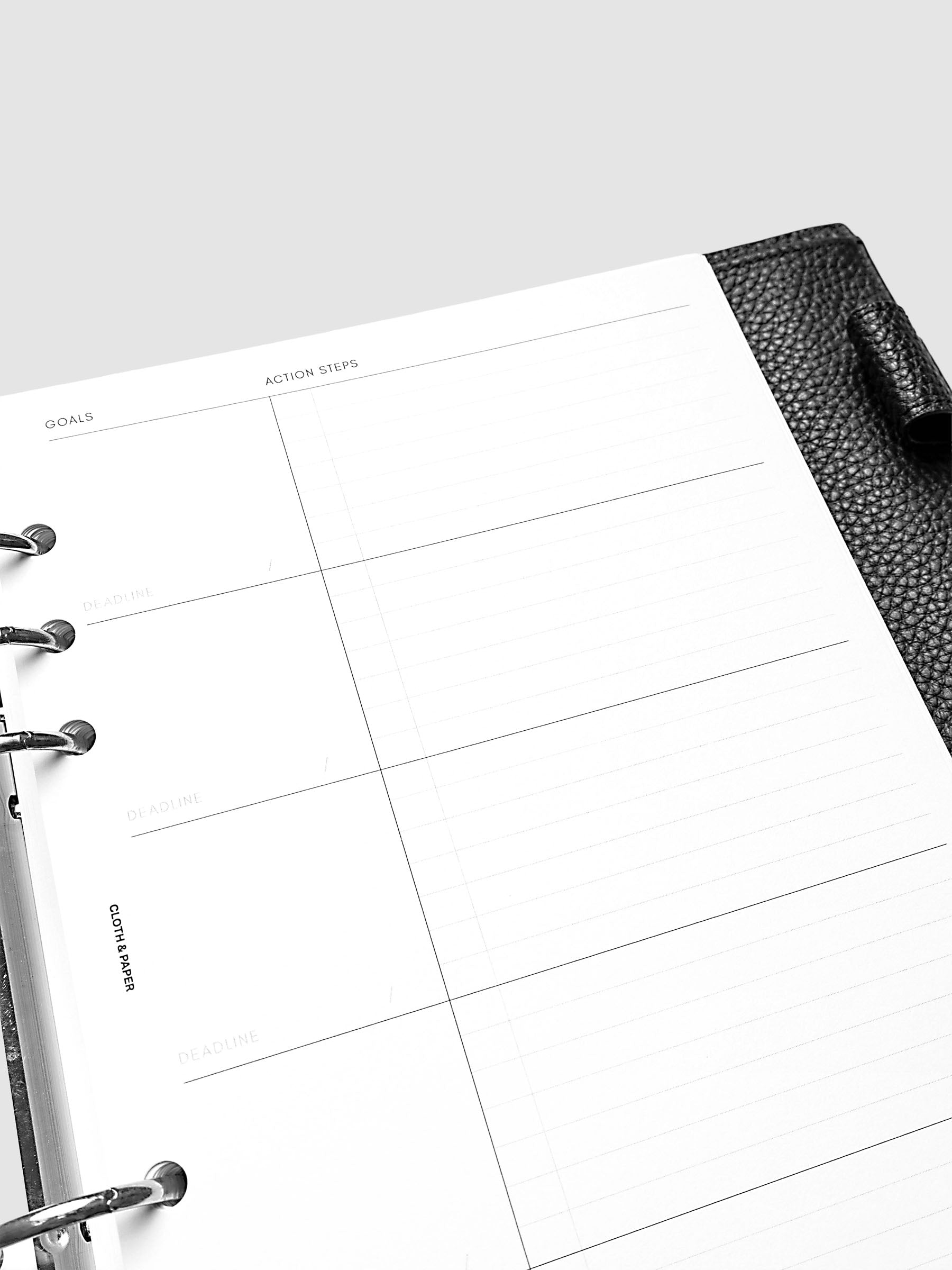 Open black leather planner displaying a blank goals and action steps worksheet with sections for deadlines and completion dates. The page is ready to be filled in for planning and organization.