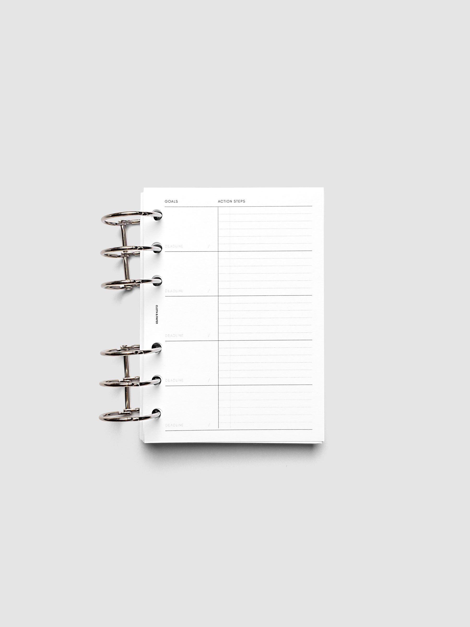 Open ring-bound planner with blank goal and action steps sections on a white page, placed on a light gray background. The planner is ready for writing and organization.