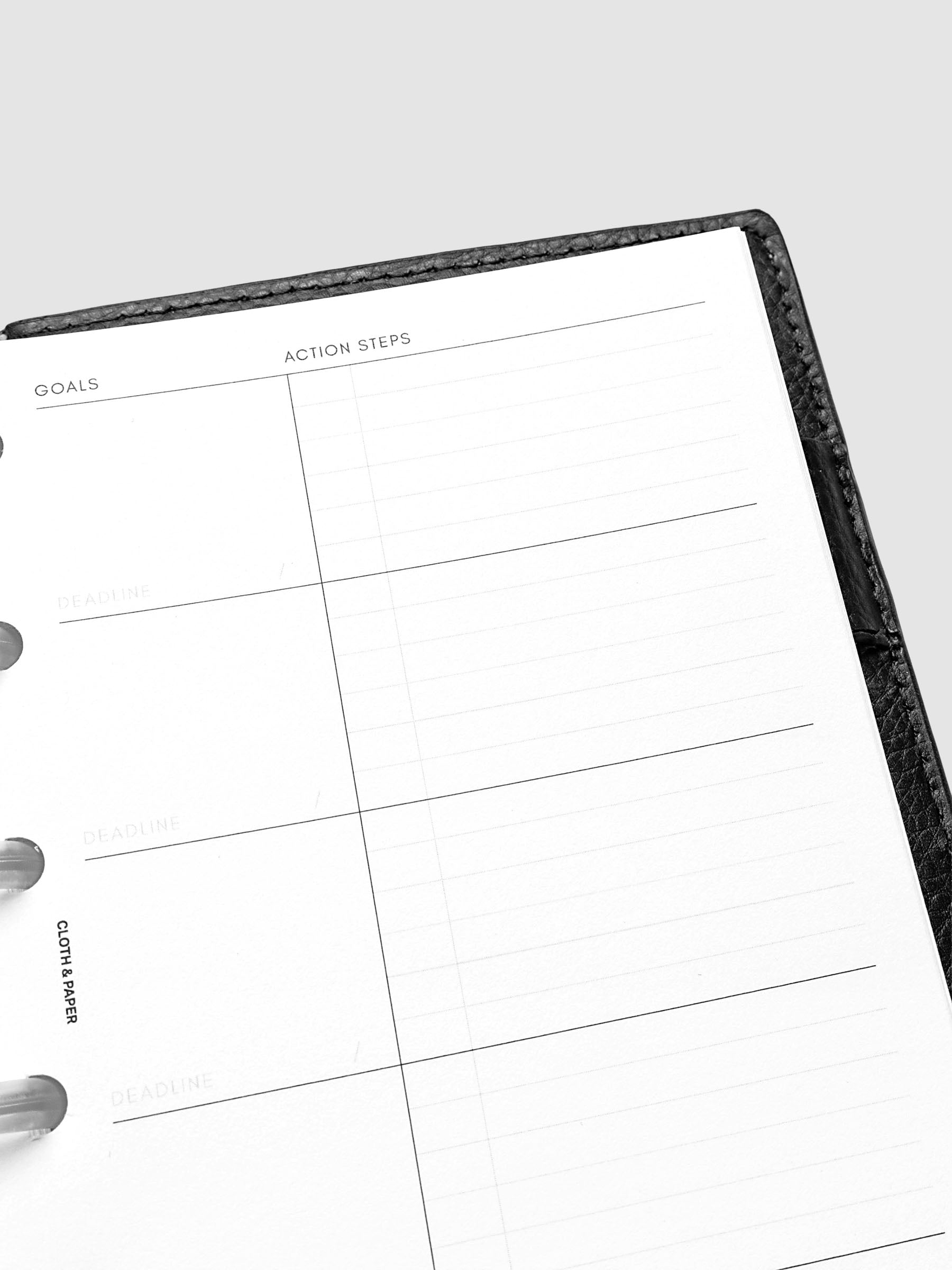 Open planner showing a blank goals and action steps page with sections for deadlines. The planner has a black cover and is photographed against a light background.