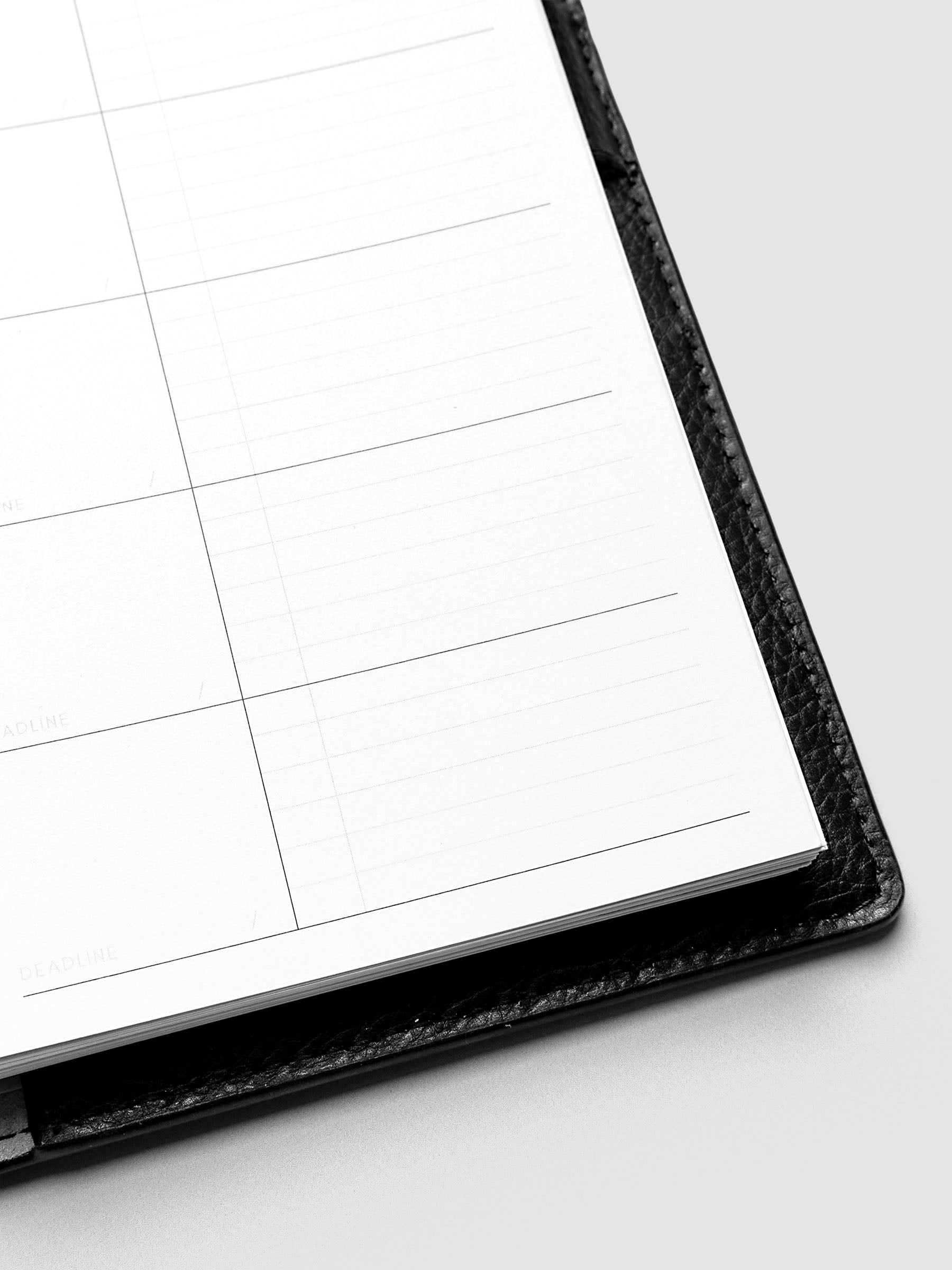 Close-up of an open planner with blank, lined pages and a black leather cover. The planner is positioned on a light gray surface.