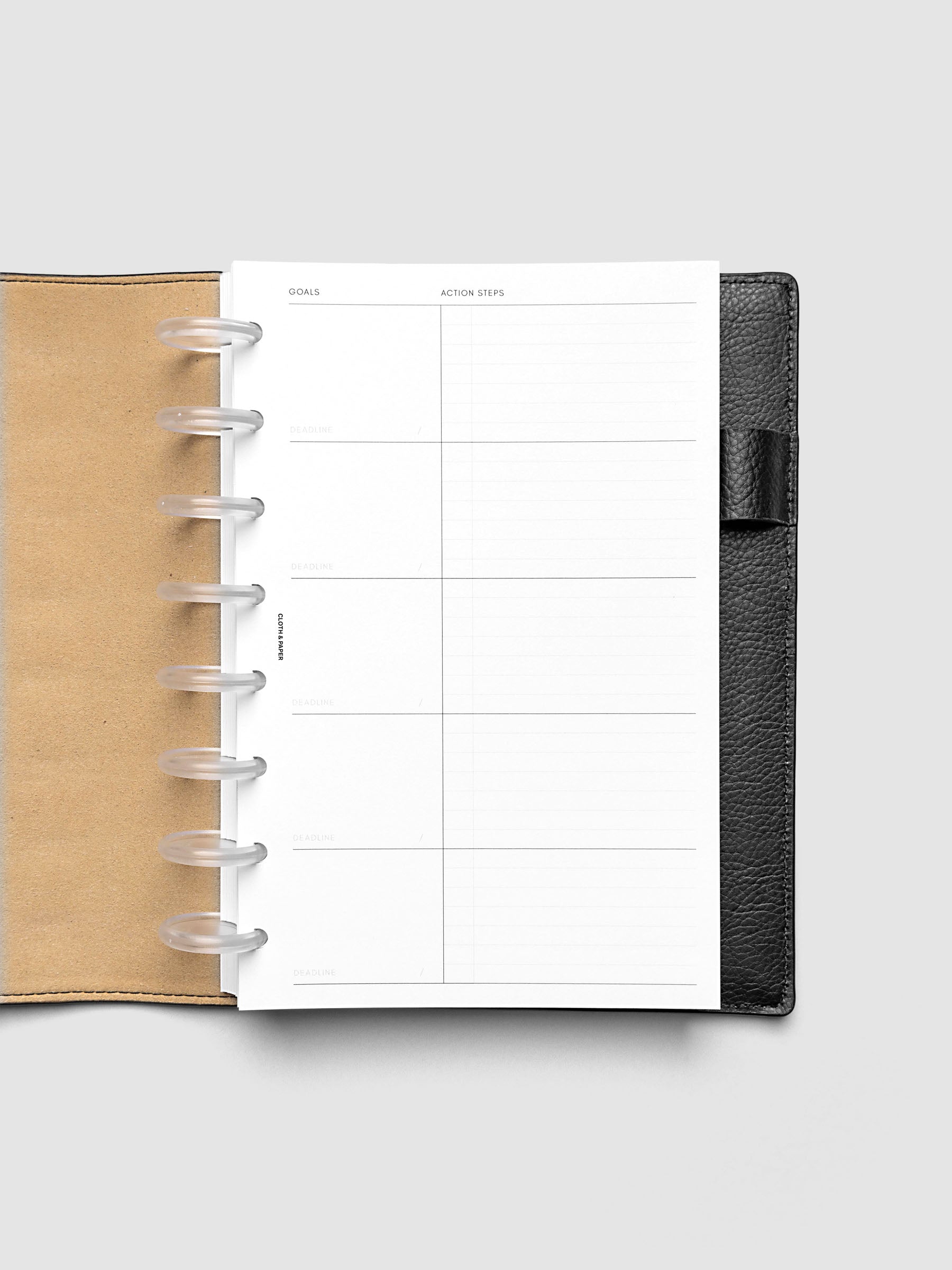Open black leather planner displaying a blank goals and action steps worksheet with lined sections. The planner is laid flat on a light gray background.