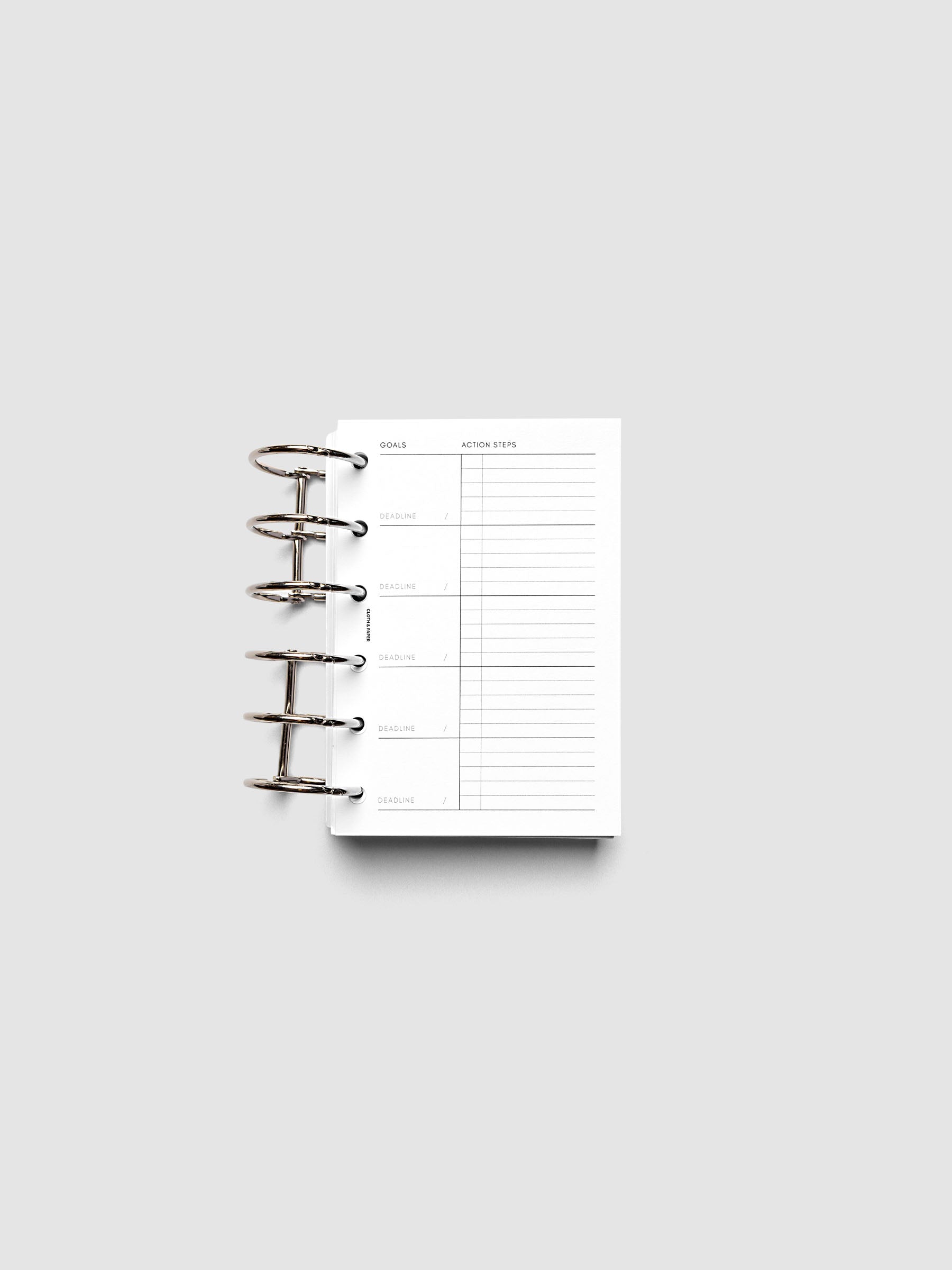 Open ring-bound planner with sections labeled "Goals" and "Action Steps" on a white background. The planner is blank and ready for writing.