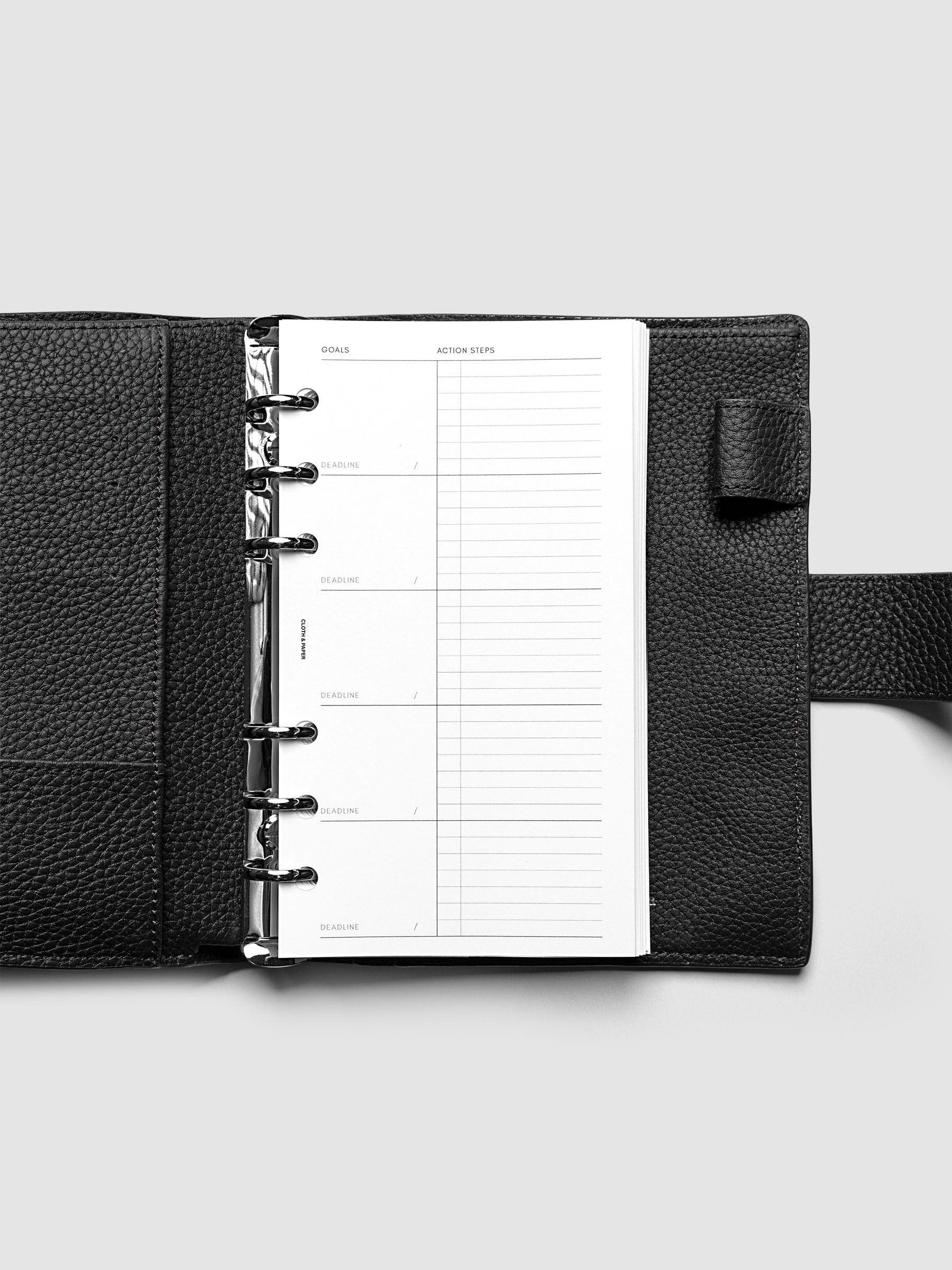 Open black leather planner displaying a blank goals and action steps worksheet. The planner is laid flat on a light gray surface.