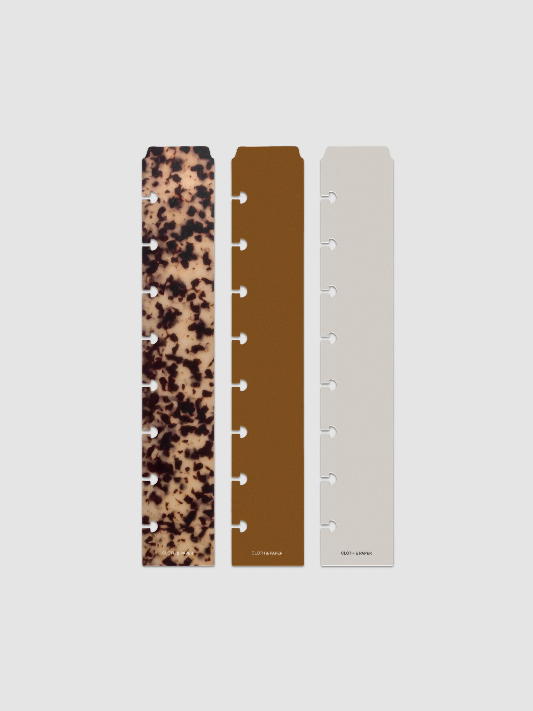 Narrow Page Marker Set Vol. 2, a set of 3 page markers for planners and notebooks shown in size Half Letter. Includes one tortoiseshell pattern, one solid brown, and one solid grey page marker.