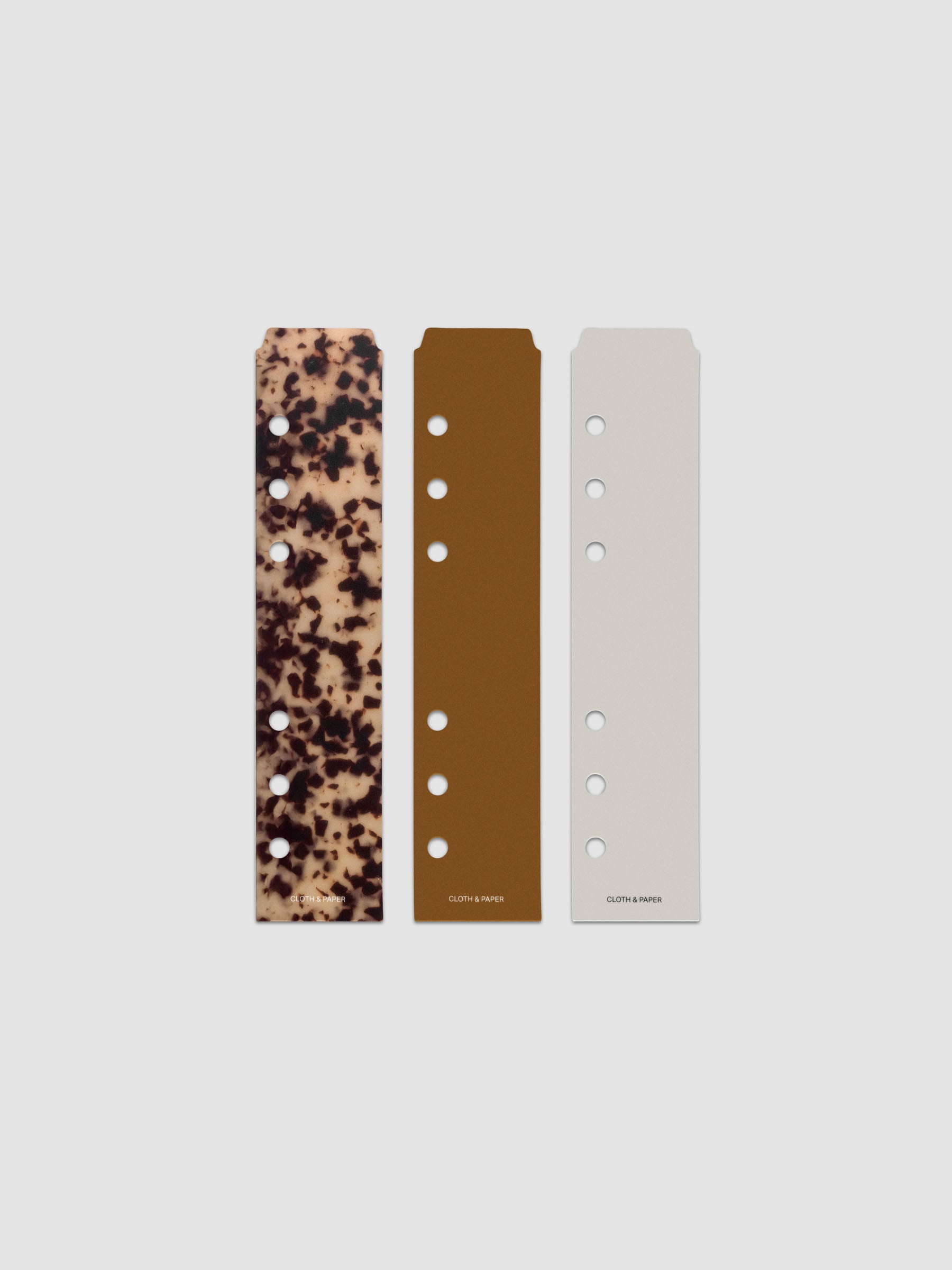 Narrow Page Marker Set Vol. 2, a set of 3 page markers for planners and notebooks shown in size Personal/Personal Wide. Includes one tortoiseshell pattern, one solid brown, and one solid grey page marker.
