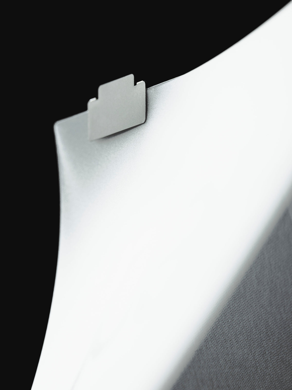 A single stainless steel Index File Tab clipped to the curved edge of a white page against a black background.