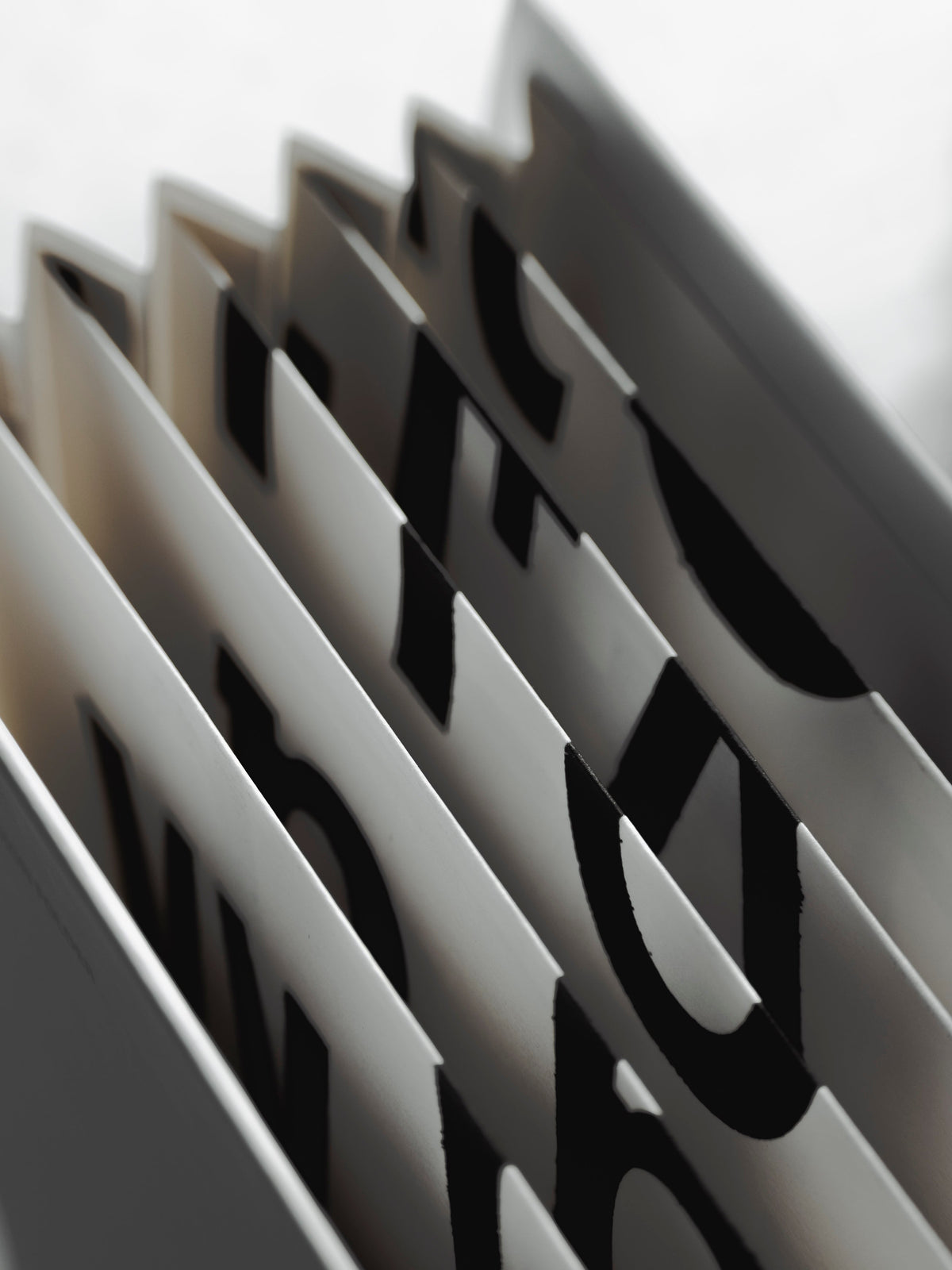 Close view inside the Editorial Accordion Folder, its fanned white pockets printed with large black letterforms.