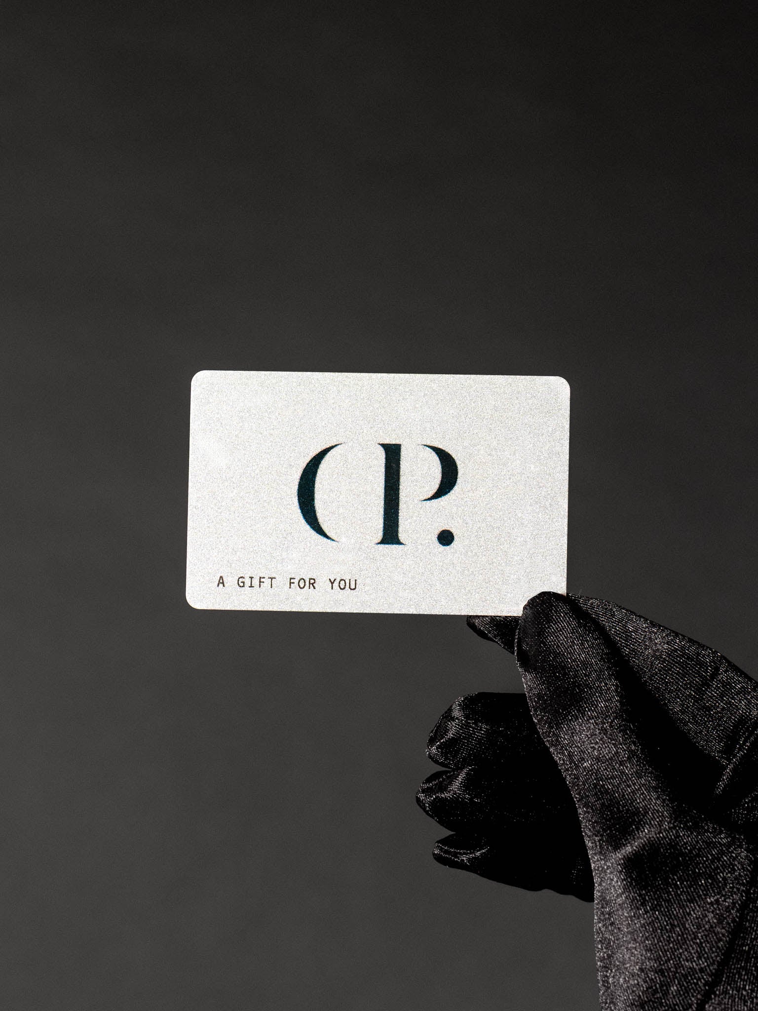 Gloved hand holding a C&P Gift card against a dark backdrop.