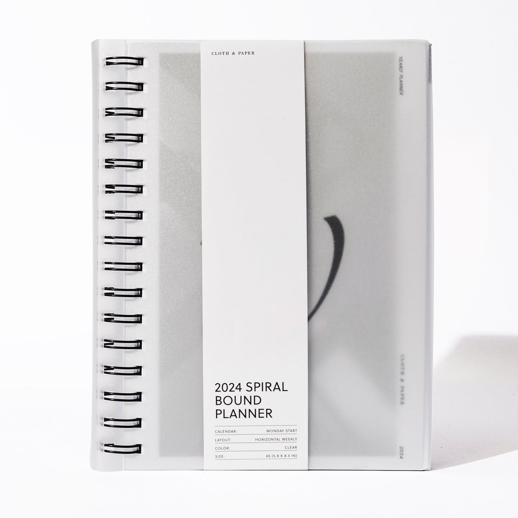 2024 Spiral Bound Planner, Horizontal Weekly, Cloth and Paper. Spiral notebook displayed with its belly band packaging on a white background.