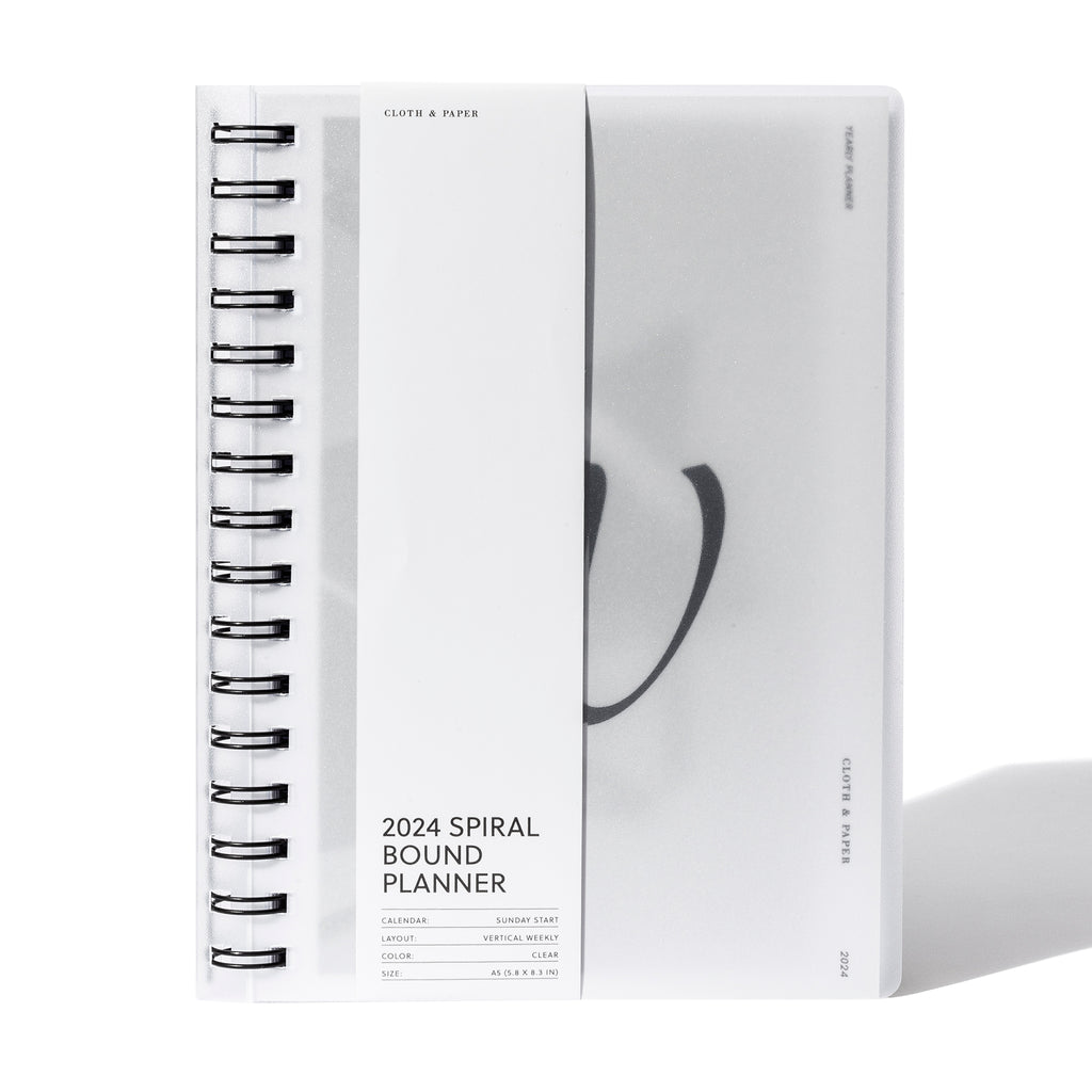 2024 Spiral Bound Planner, Vertical Weekly, Cloth and Paper. Spiral notebook displayed with its belly band packaging on a white background.