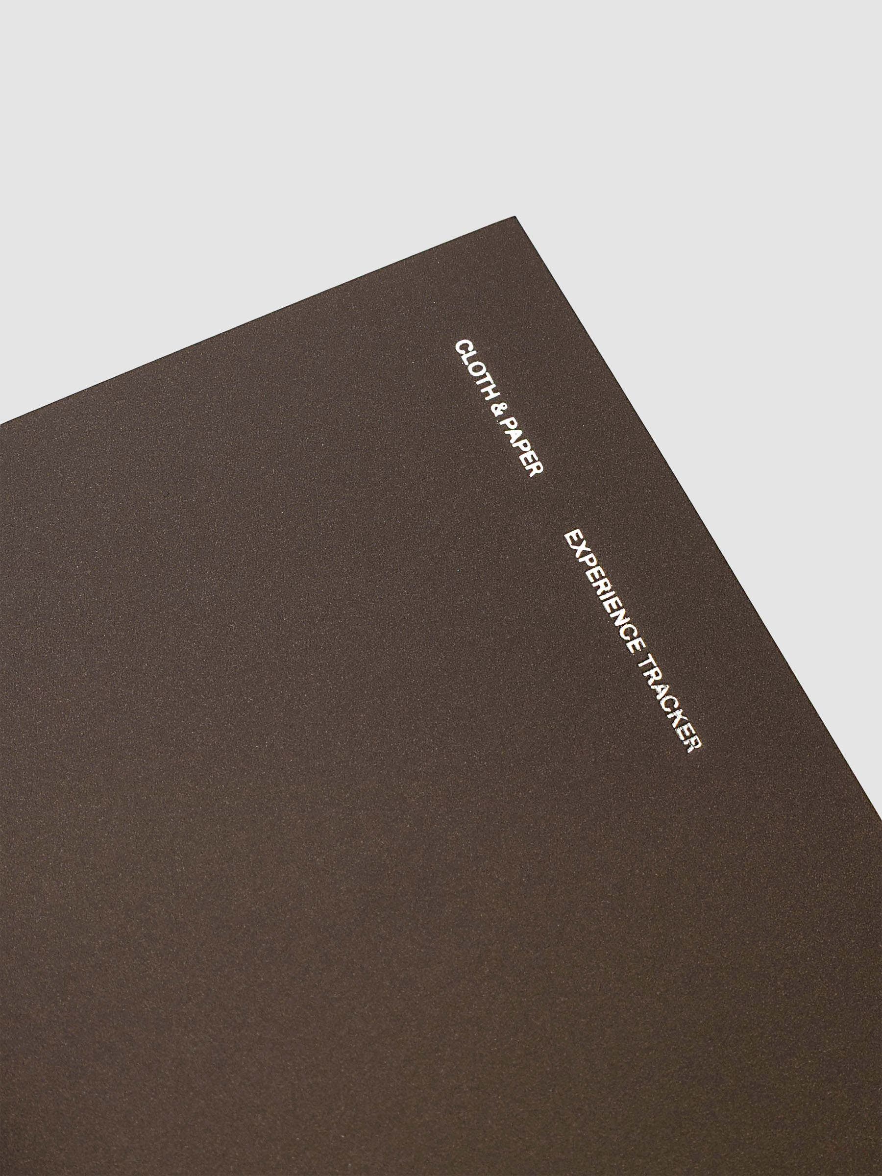 Close up image of the Experience Tracker Walnut Pocket Plus notebook from the Traveler's Notebook Collection. The cover has gold foil text that reads Cloth and Paper Richmond, VA Monthly Admin and is displayed on a neutral background