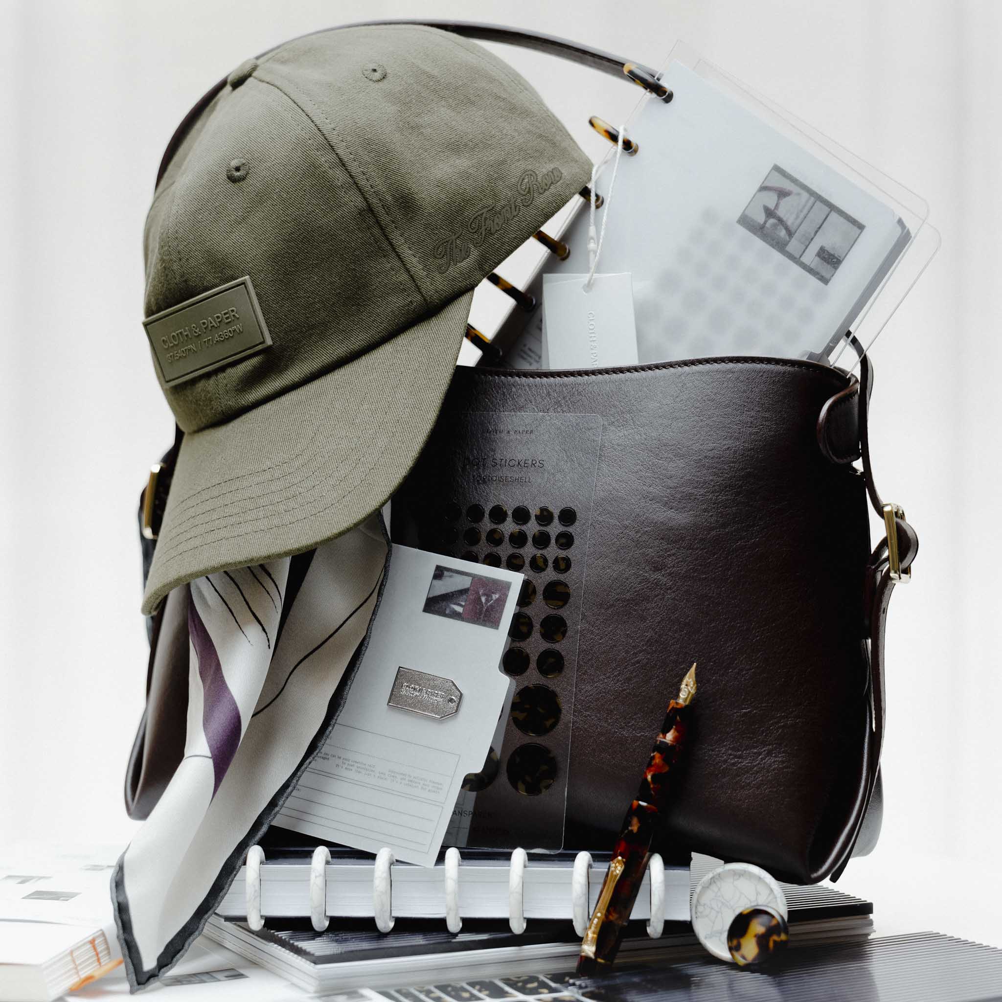 Several Planner Essentials and accessories from the Front Row Collections staged inside a Valencia Bag.  Heavily featured are the Label Hat, Planner Brooch | Tag, and Kaweco Art Sport Fountain Pen in Hickory Brown.