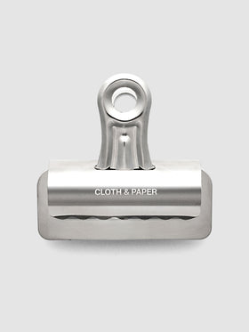 Silver metal notebook clip with Cloth & Paper logo etched onto the surface.