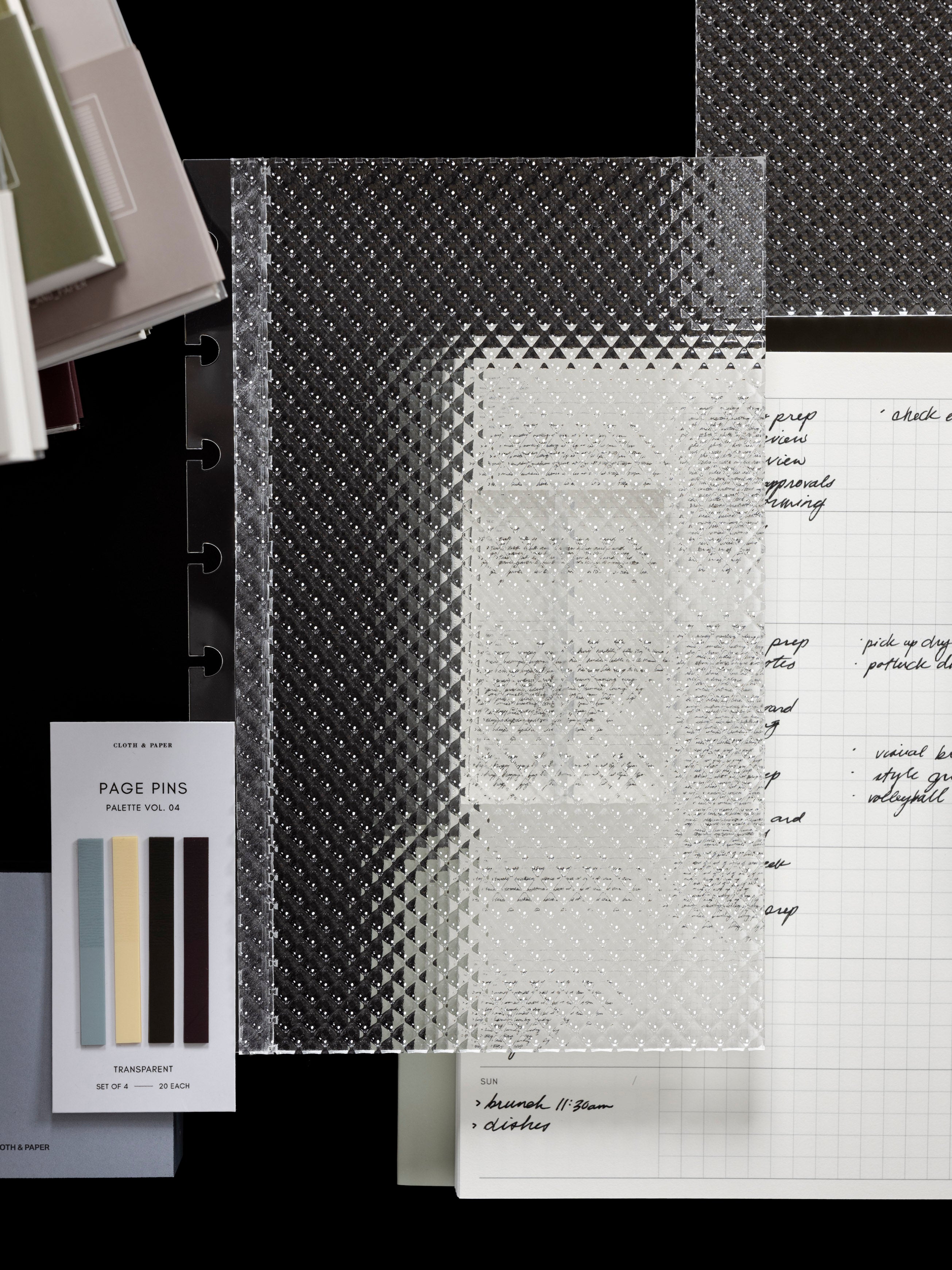 Clear, transparent, textured Studded Planner Dashboard shown in size Half Letter in front of a variety of products on a dark background.