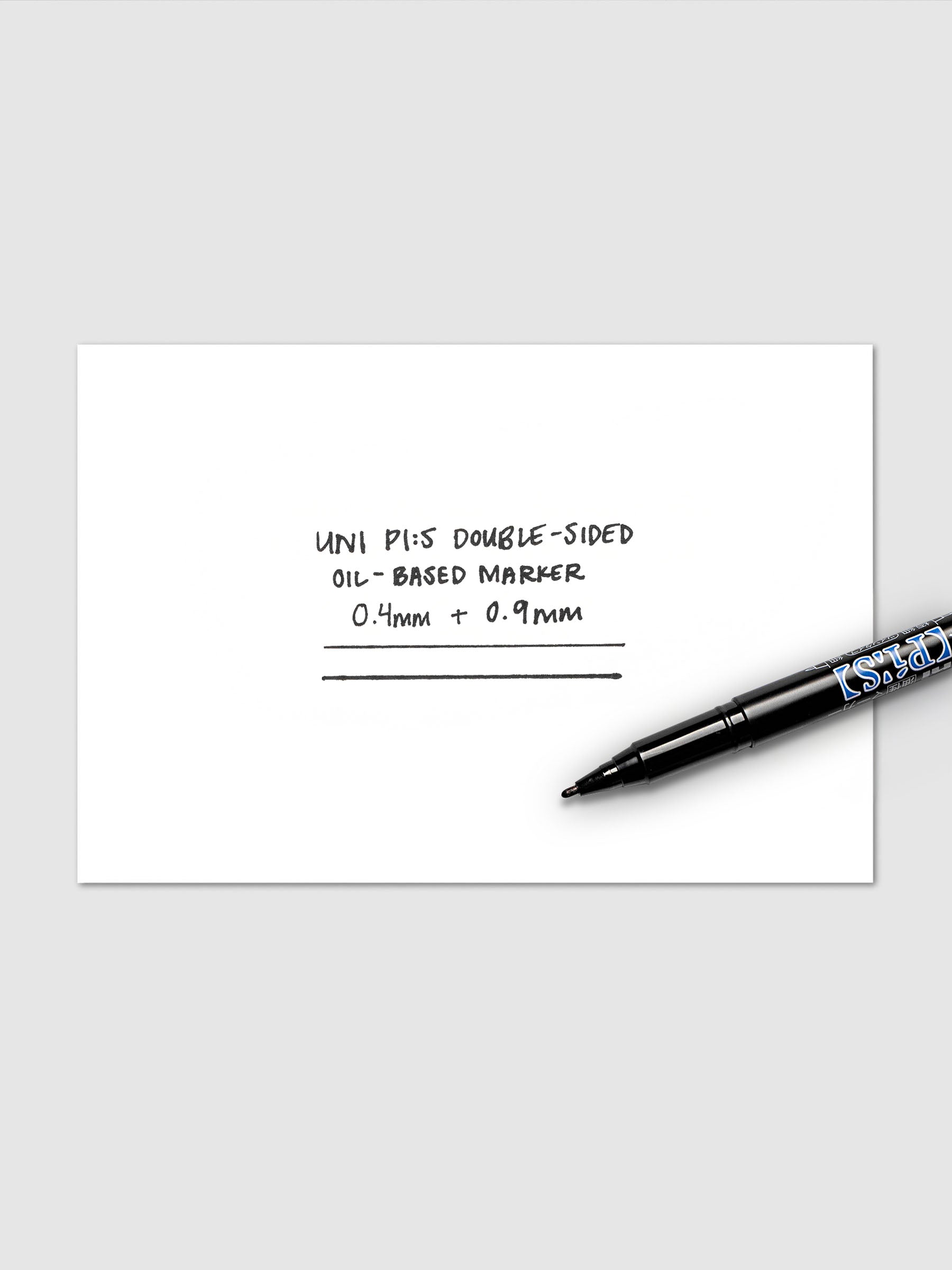 White card with 0.4 mm and 0.9 mm marker writing samples with black marker laying on top.