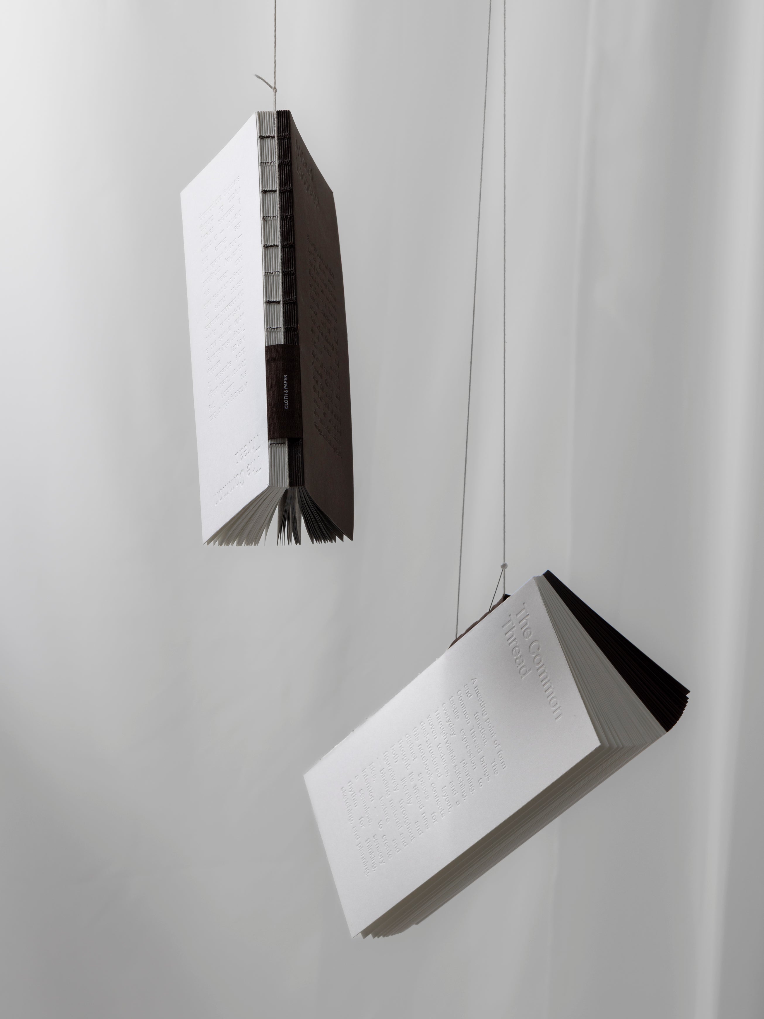 Two Common Thread Notebooks hanging from string against a white fabric background.