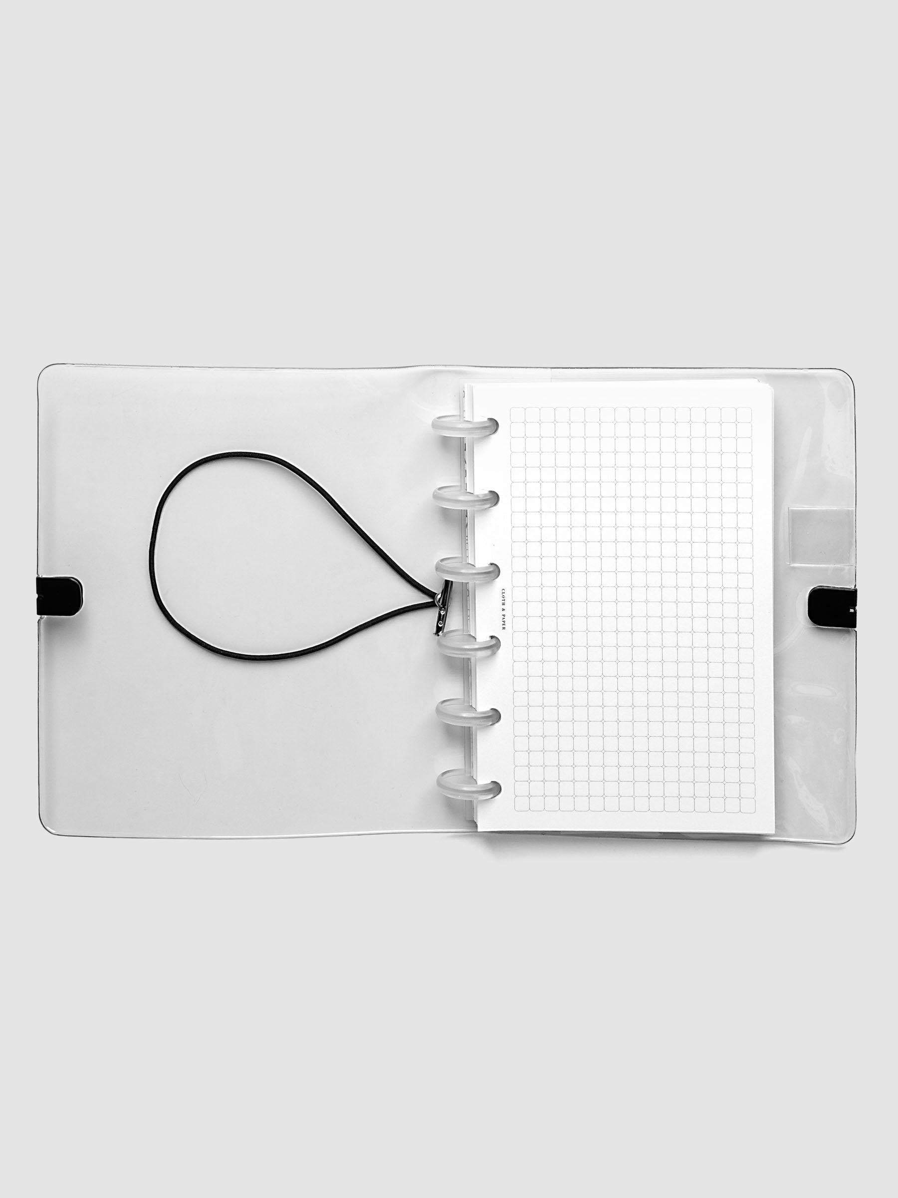Clear Vinyl Planner Cover in size CP Petite shown open with a discbound planner inside on a grey background.