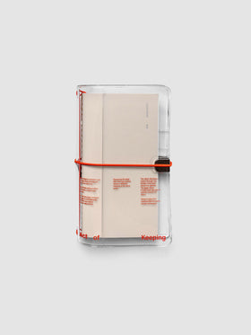 Act of Keeping Travel Notebook Cover in clear vinyl with deep orange bands, shown holding travel notebooks