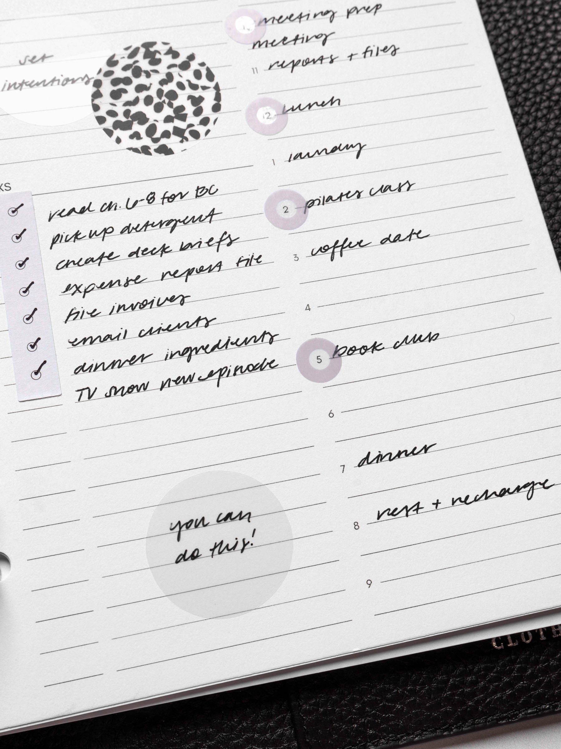 Closeup of inserts in use inside a leather planner. They are filled out with sample text and have been decorated with Spotlight stickers, Strips planner stickers, and a transparent Circle Page Flag.
