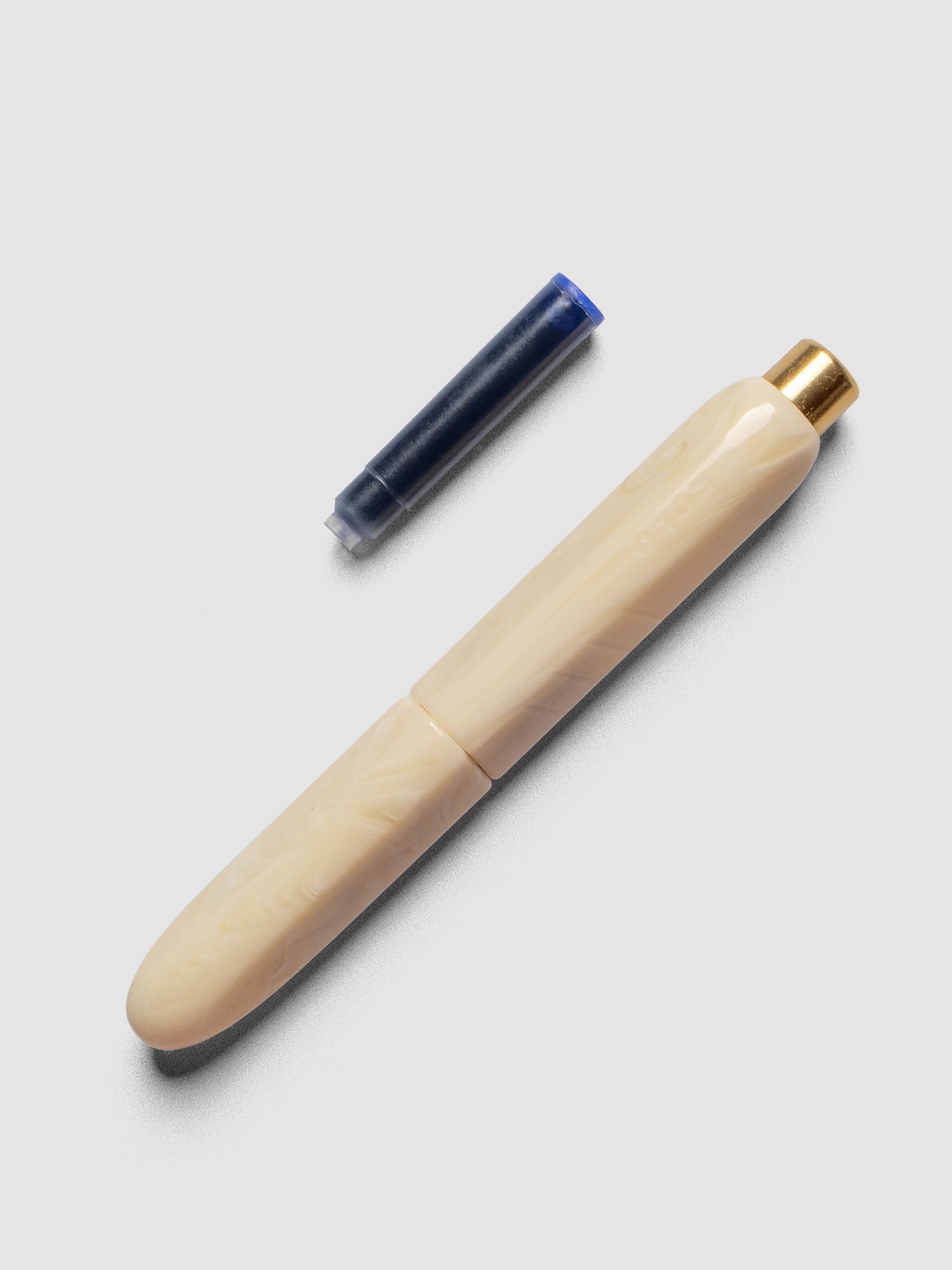 Kolo Tino Fountain Pen in the color Mother, a warm beige barrel with brass accents and a silver medium nib. Shown with cap on and the ink cartridge beside the pen.