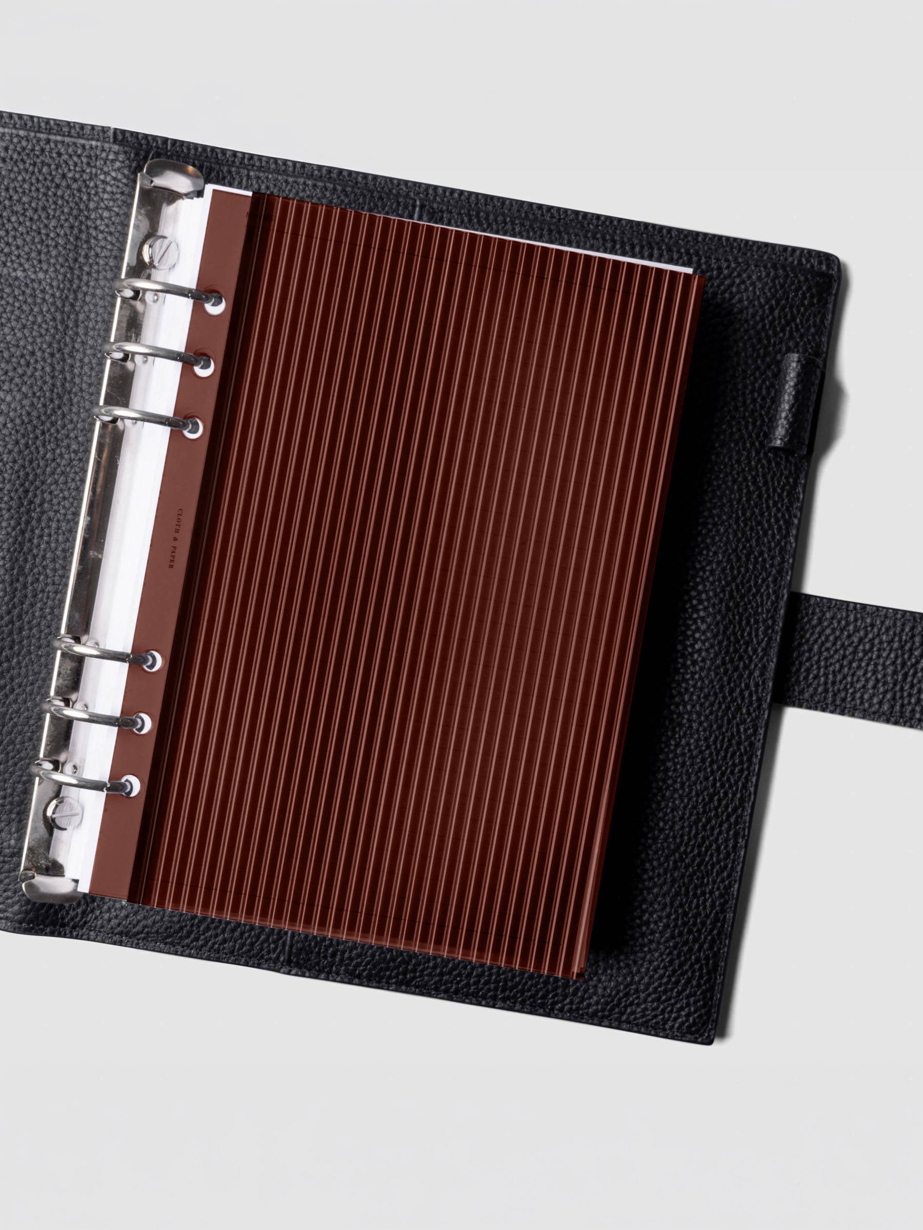 Bordeaux fluted planner dashboard in A5 size shown in a black leather six ring agenda with silver rings.