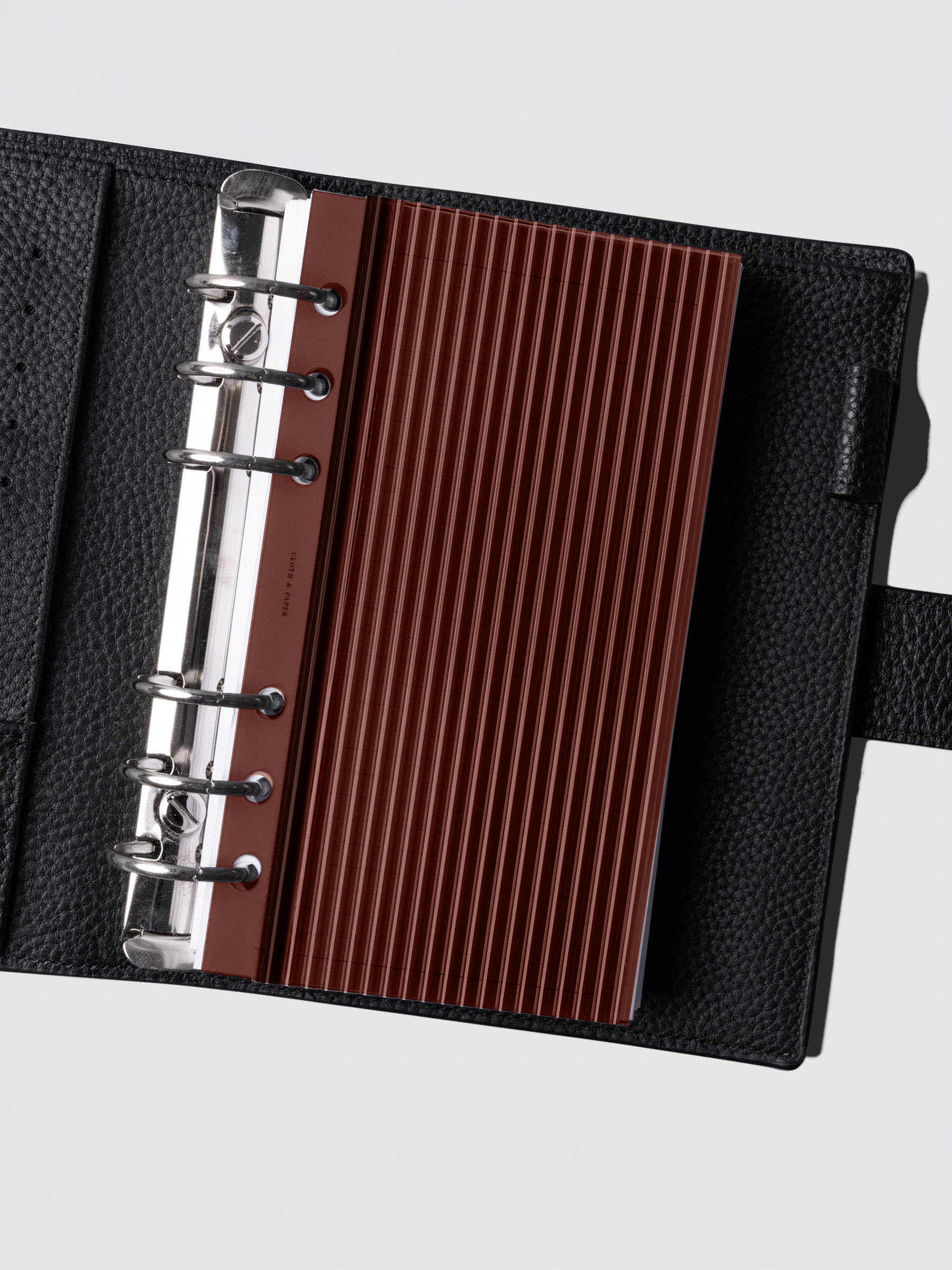 Bordeaux fluted planner dashboard in Personal size shown in a black leather six ring agenda with silver rings.