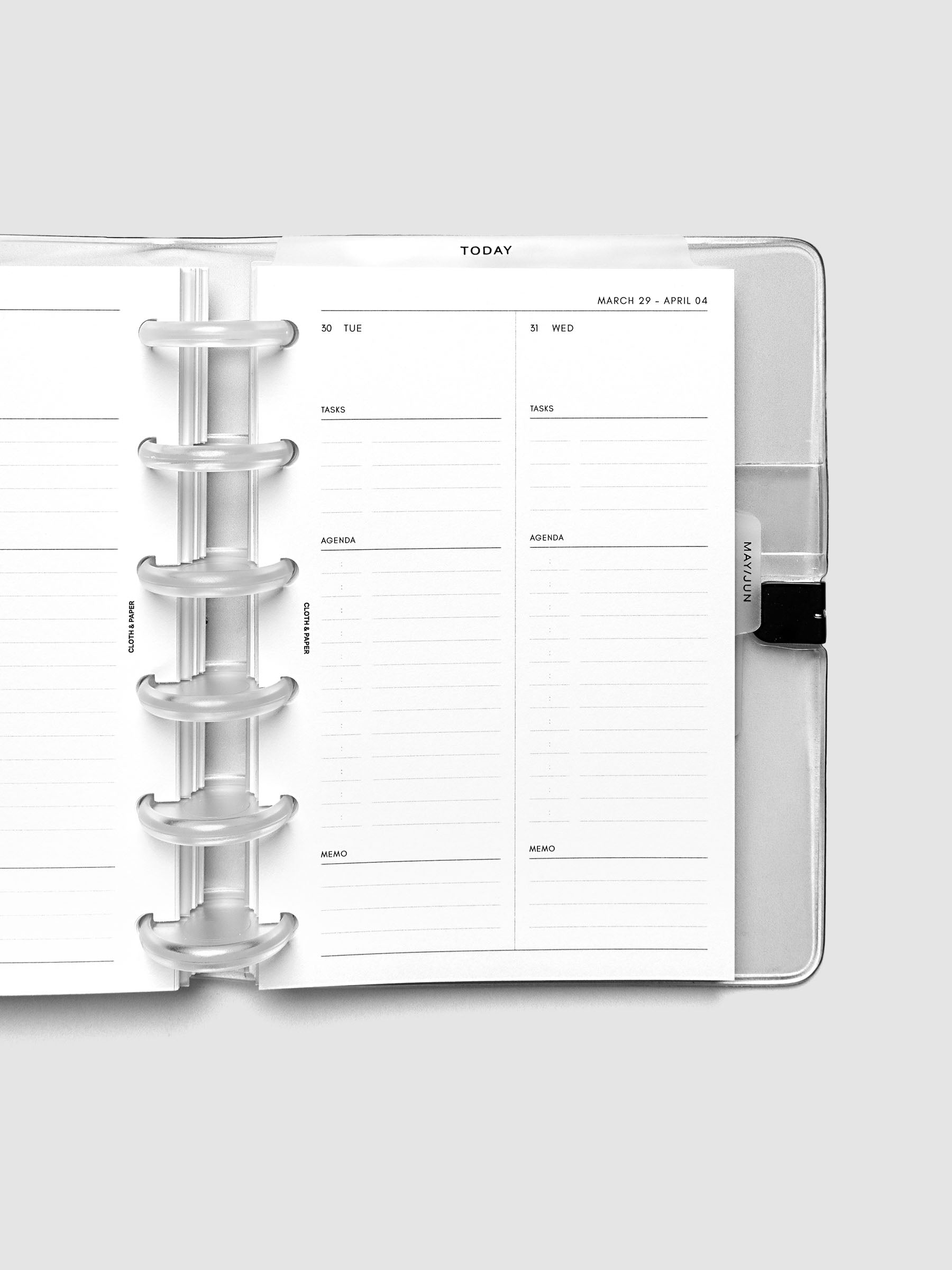 Close-up of an open planner with clear 6-disc binding, weekly spread showing Tuesday and Wednesday daily columns with tasks, agenda, and memo sections, tabbed monthly dividers visible at the edge, CP Petite 6-Disc Punch size